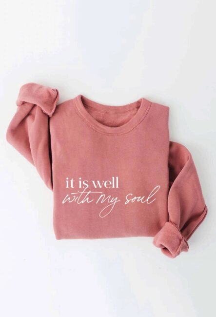 Pink sweatshirt with the phrase "it is well with my soul" in white script on the front. Sleeves are casually rolled up.