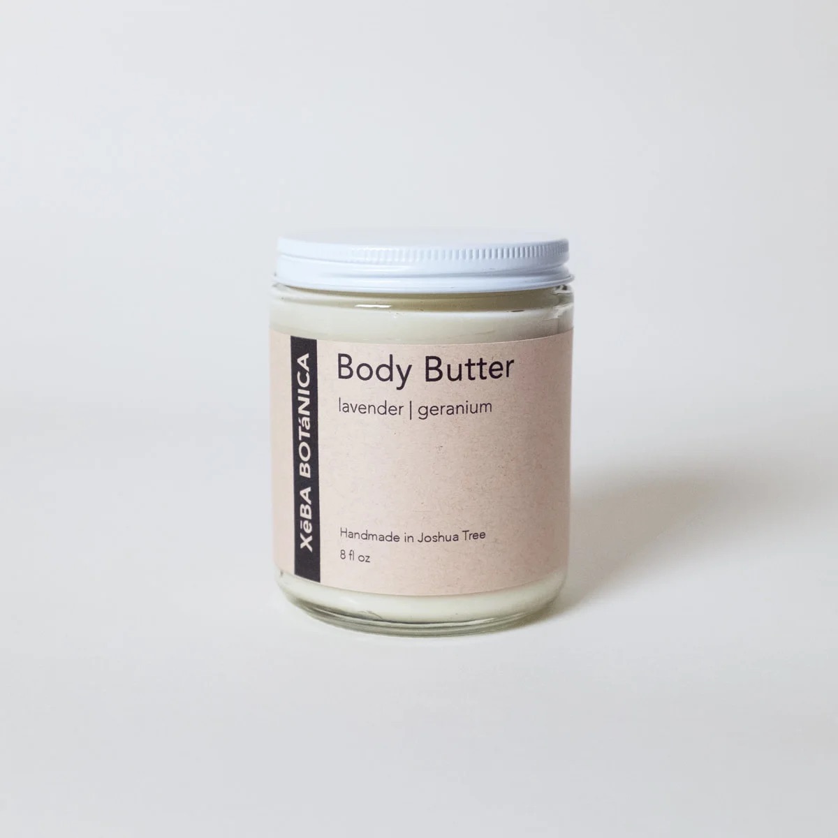 A jar of body butter labeled "lavender | geranium" from XBBA Botanica, 8 oz, with a white lid on a plain background.