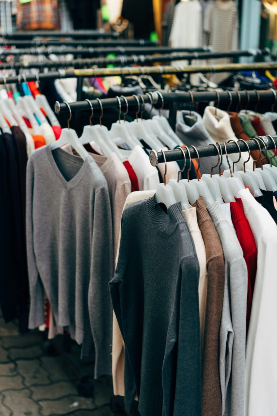 Clothes rack displaying a variety of sweaters in different colors, including gray, beige, red, and white, on hangers in a store setting.