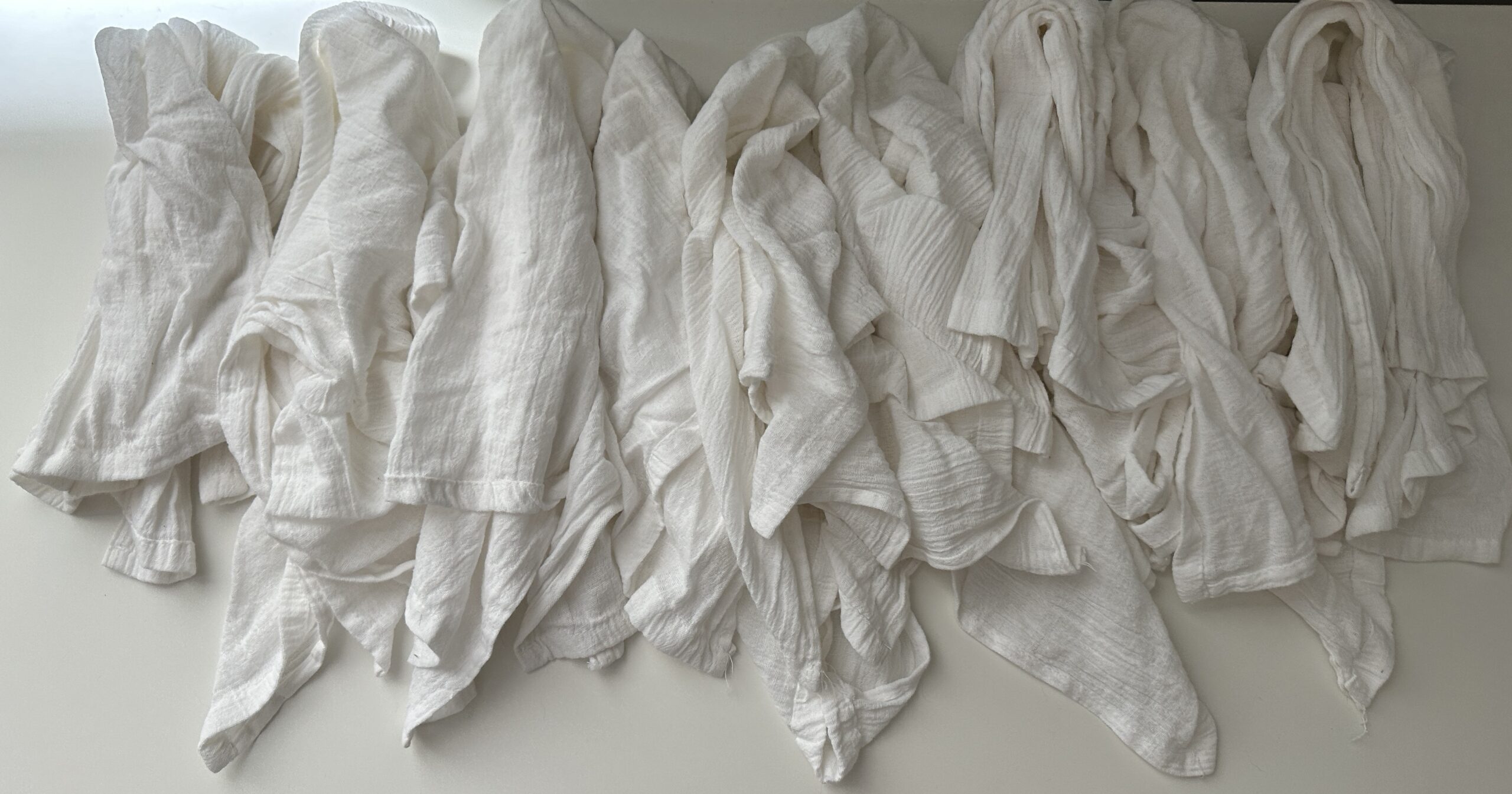 White, crumpled fabric pieces laid out in rows on a flat surface.