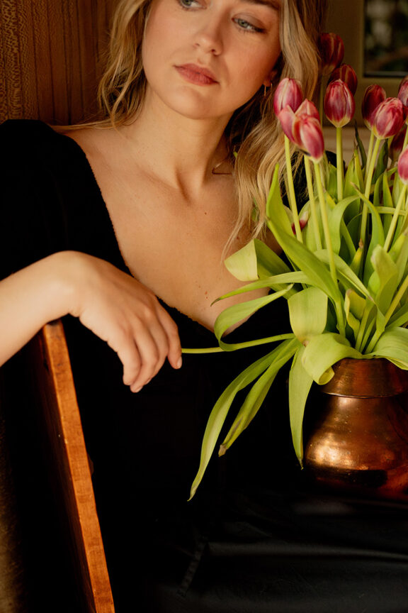 A person in a black shirt sits beside a vase of tulips.