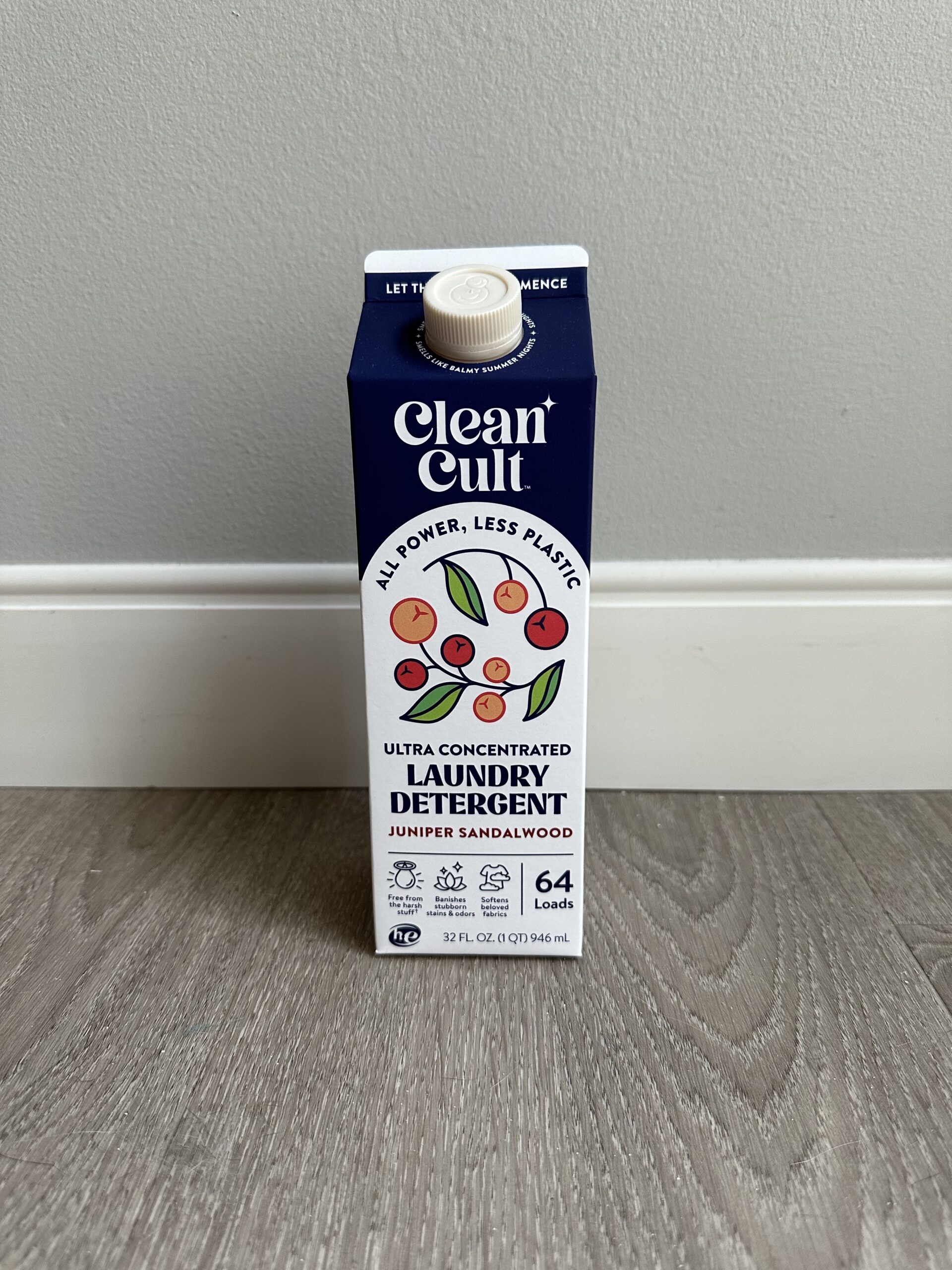 A 32 oz carton of Clean Cult ultra concentrated laundry detergent in juniper sandalwood scent, placed on a wooden floor against a gray wall.