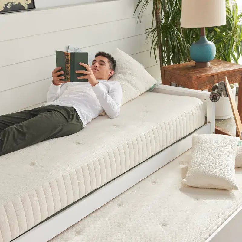 A person lies on a bare Avocado mattress reading a book. 