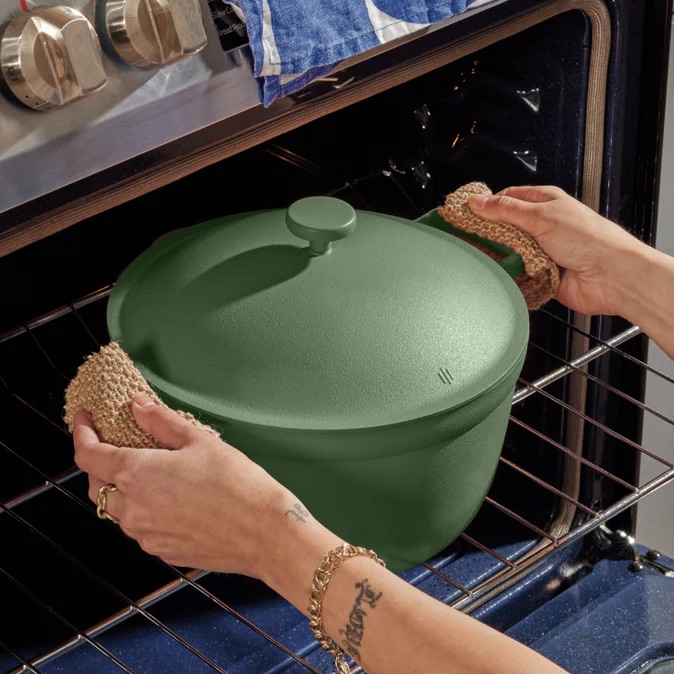 Hands wearing knitted gloves place a green pot with a lid into an oven.