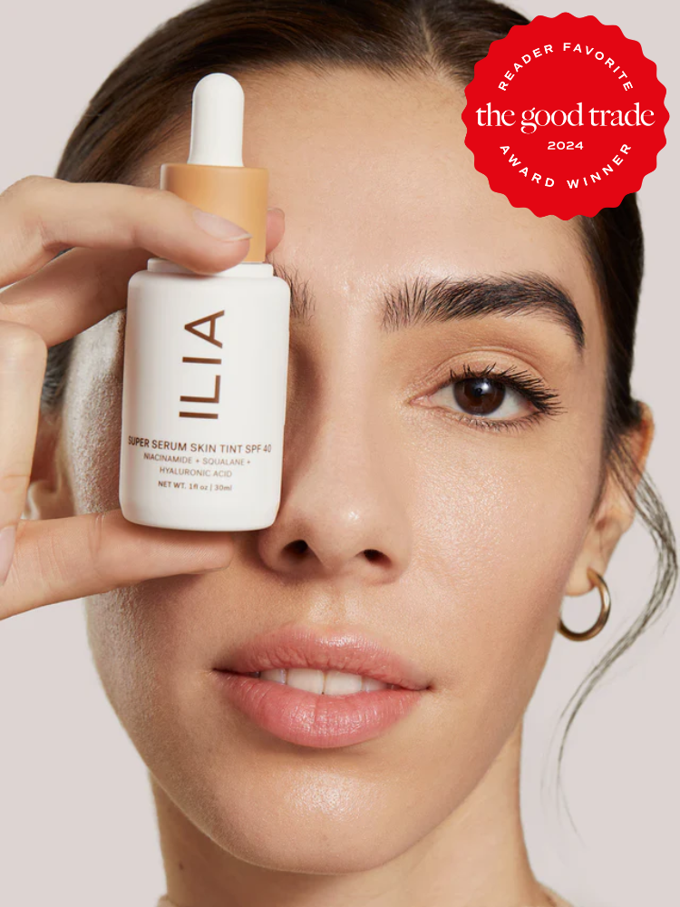 Person holding a bottle of ILIA Super Serum Skin Tint SPF 40 near their face, displaying a 2024 Good Trade award badge.