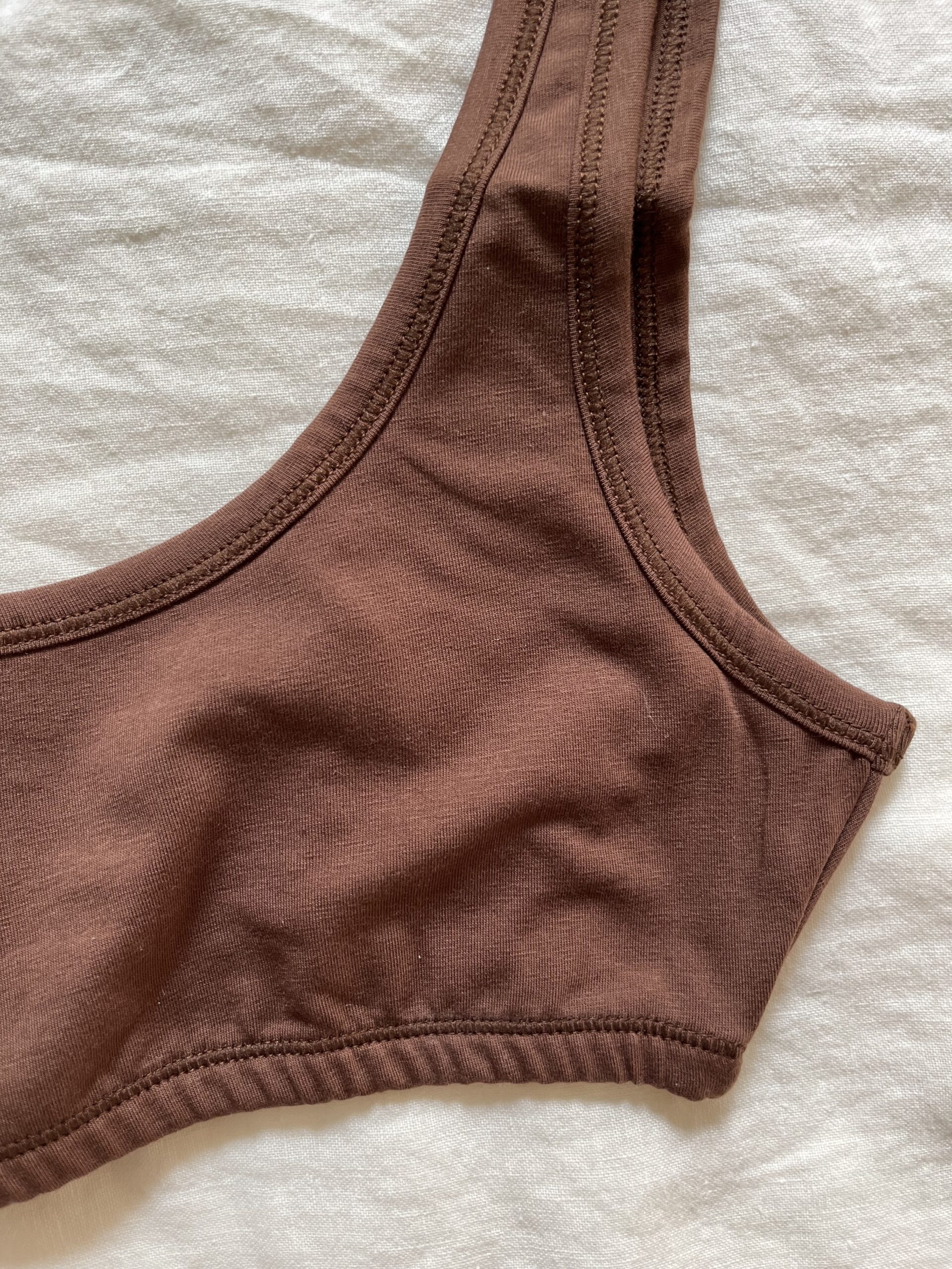 A close-up of a brown bralette laying flat on a white textured surface.