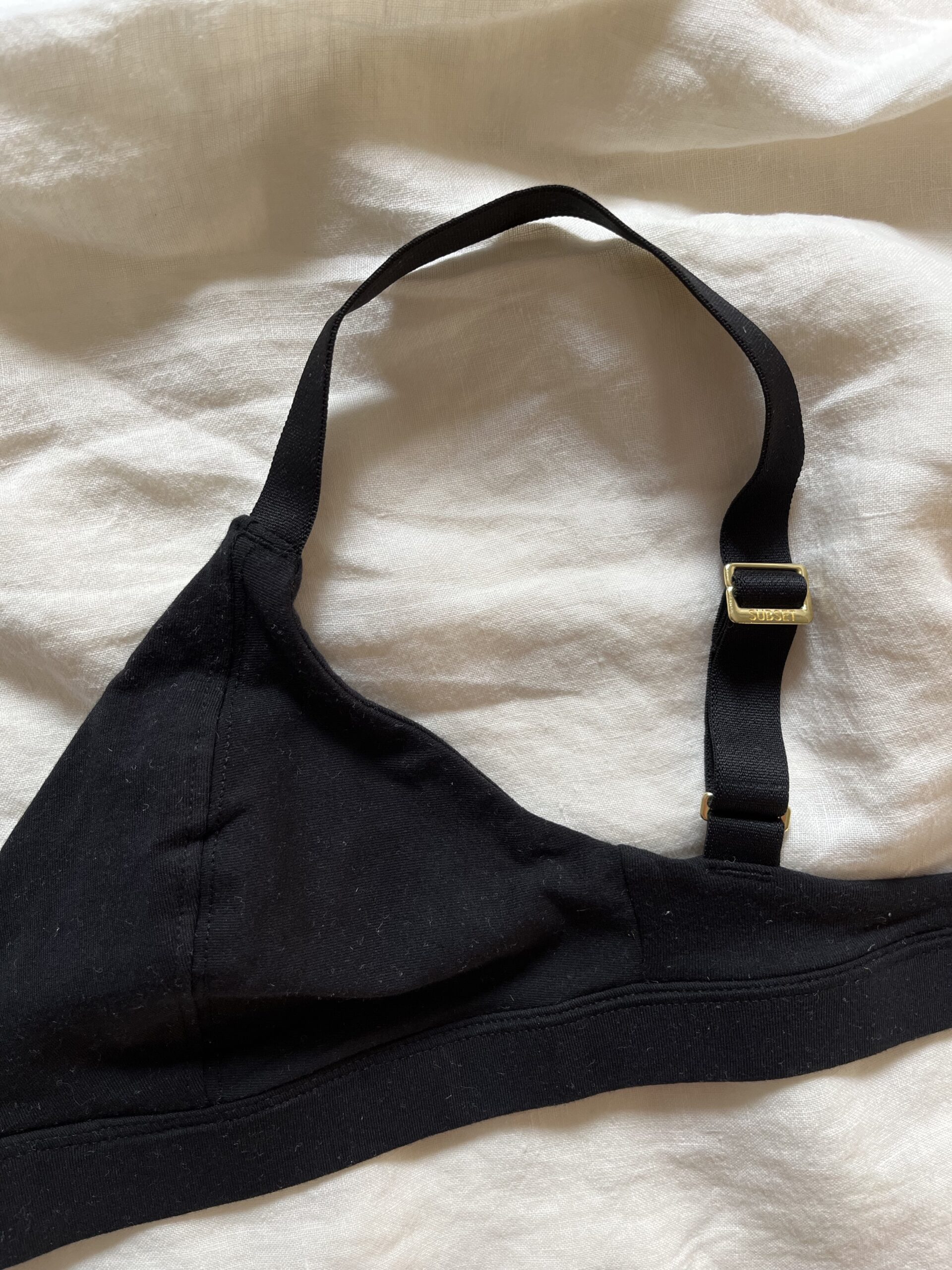 Black triangular bra with an adjustable left strap, displayed on a white fabric background.