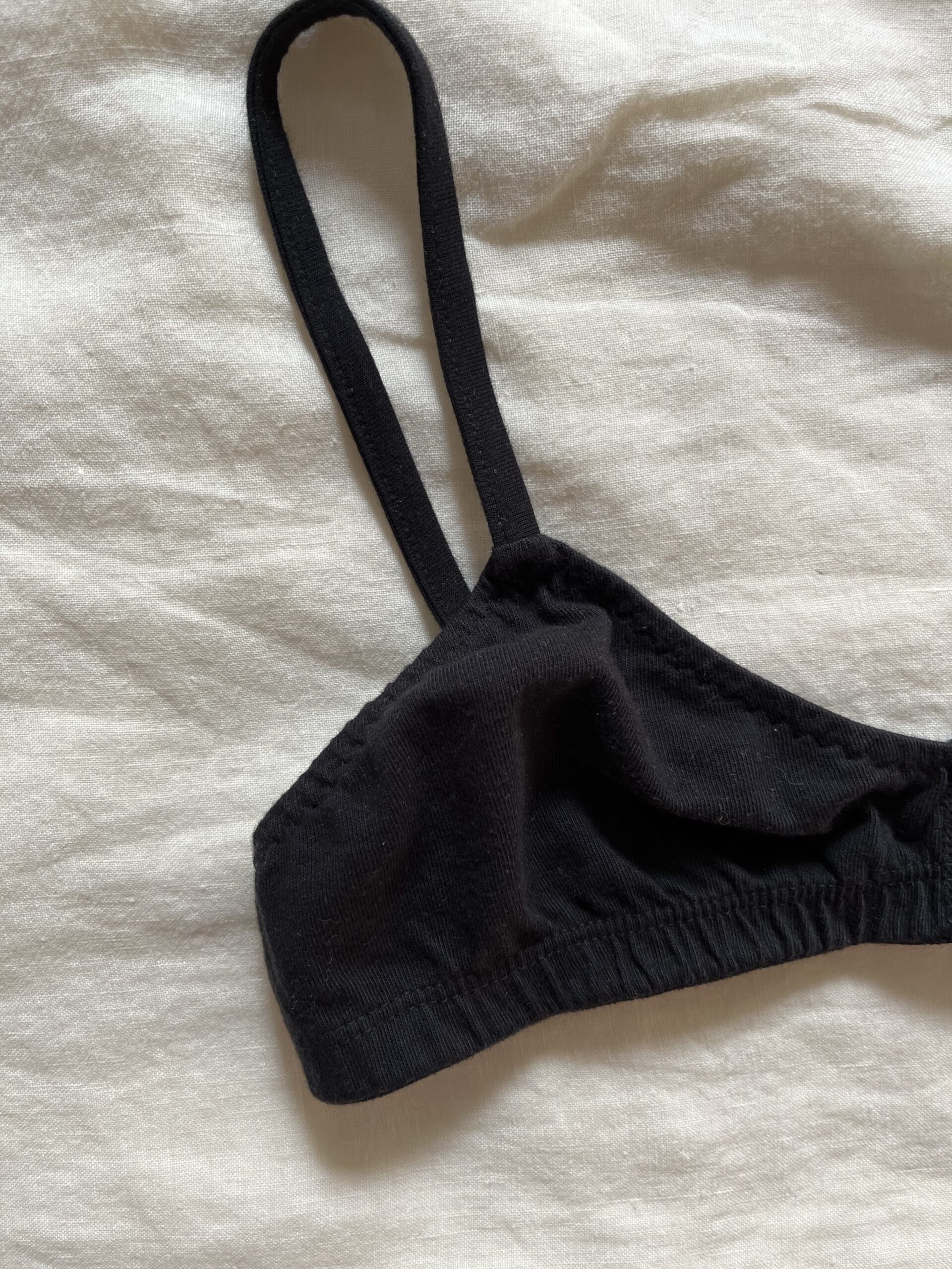 A black bralette with adjustable straps laid on a beige fabric background.