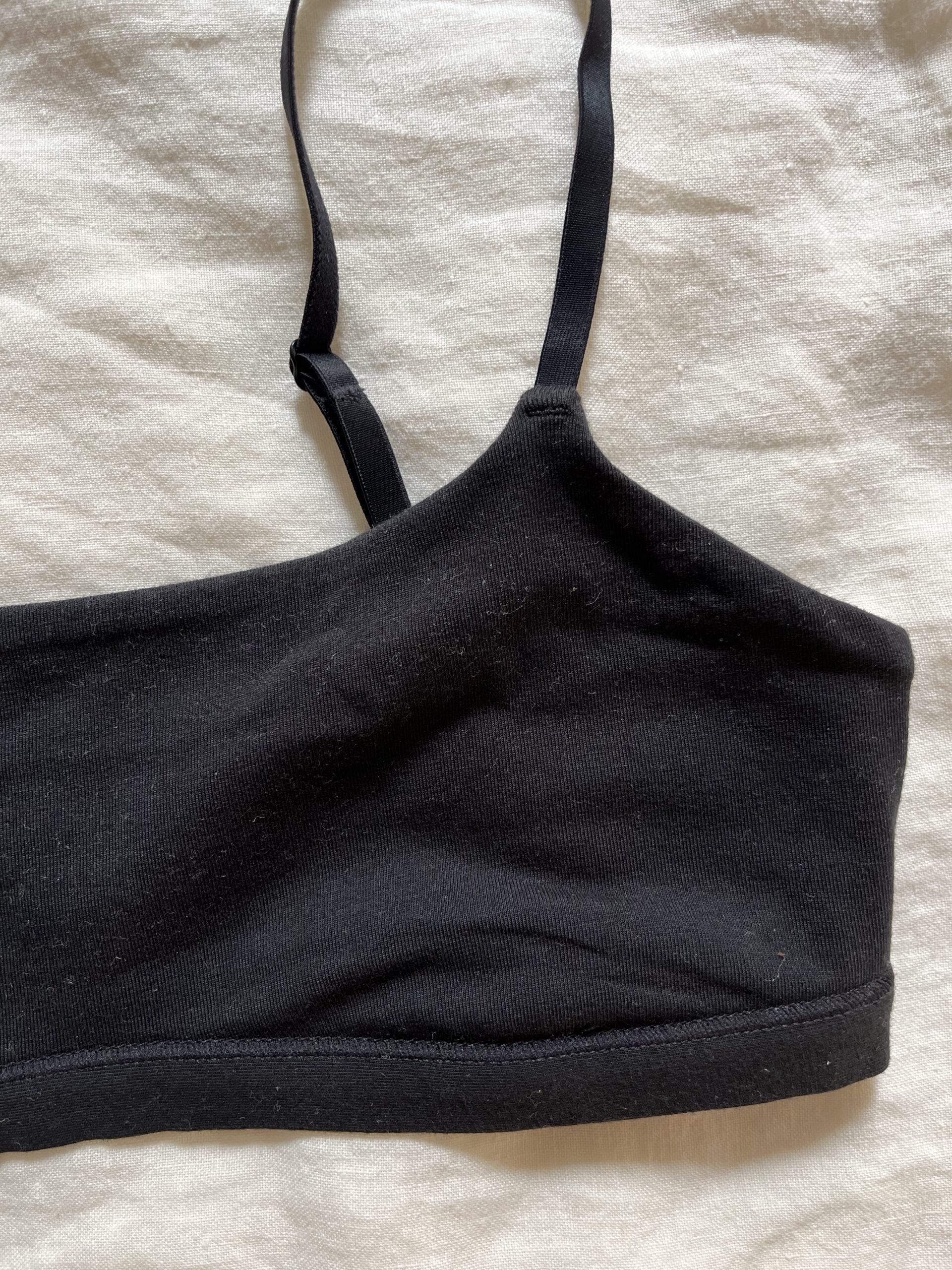 A black, single-strap crop top lies flat on a white textured surface.