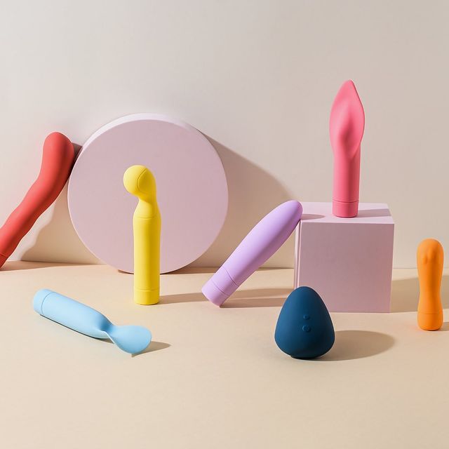 A variety of colorful vibrators and sex toys are arranged on a beige background with pink circular and square platforms.