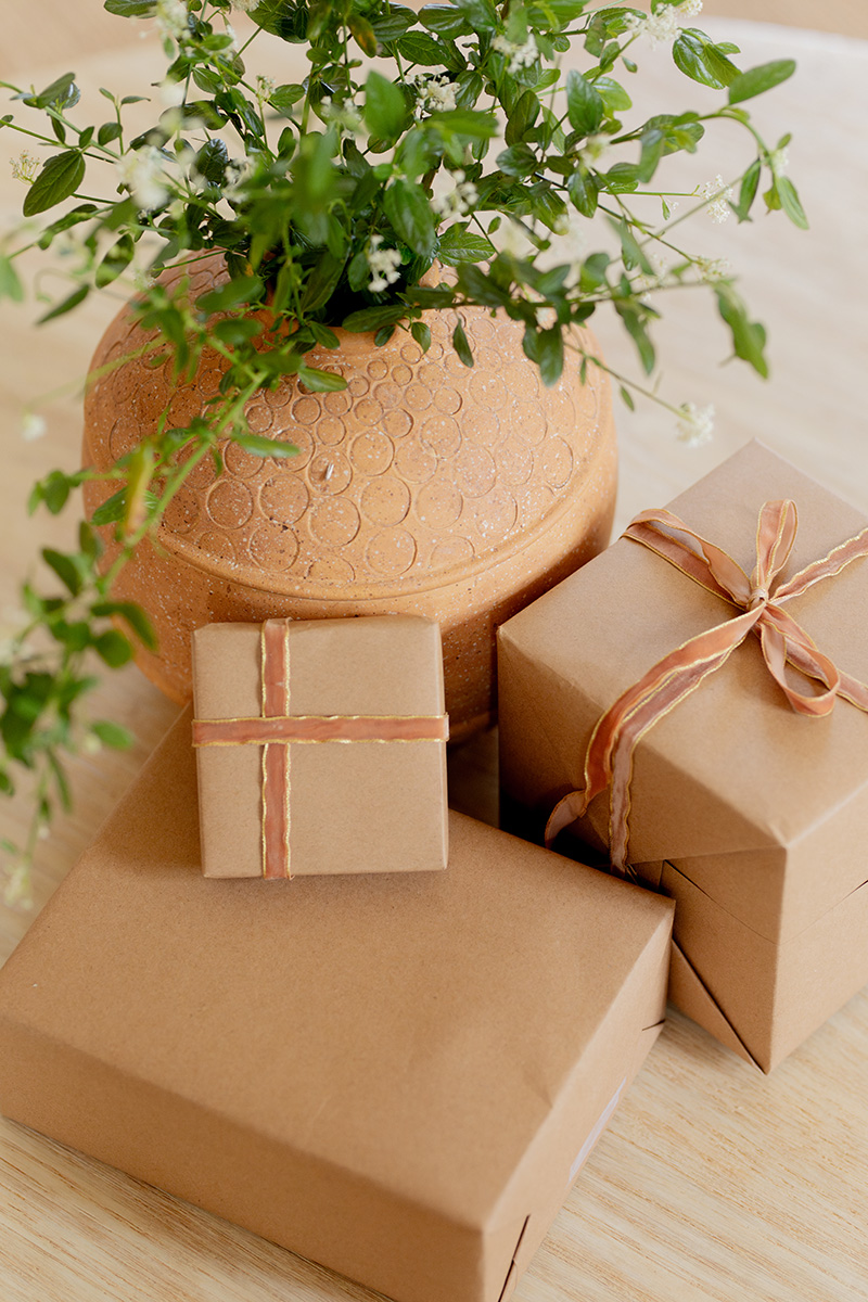 A stack of gifts set next to a plant.