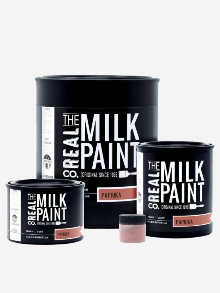 Three containers of The Real Milk Paint in paprika color, including a large can, a medium can, and a small jar of tint seal, all with black labels and white text.