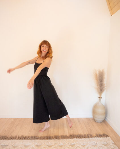 A woman in a black jumpsuit standing in a room.