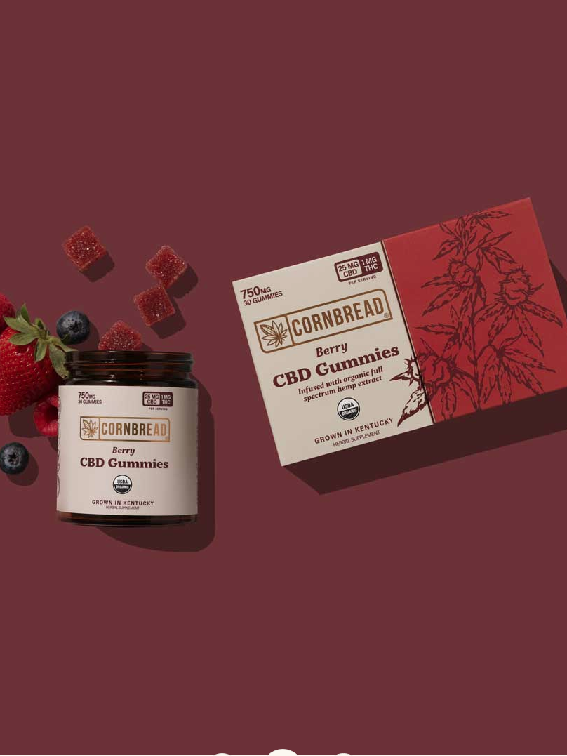 Cbd gummies from "cornbread" brand displayed with its packaging and scattered berries on a maroon background.