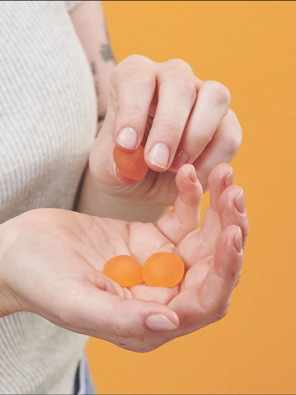A person holds three orange lozenges in their cupped hands against an orange background.