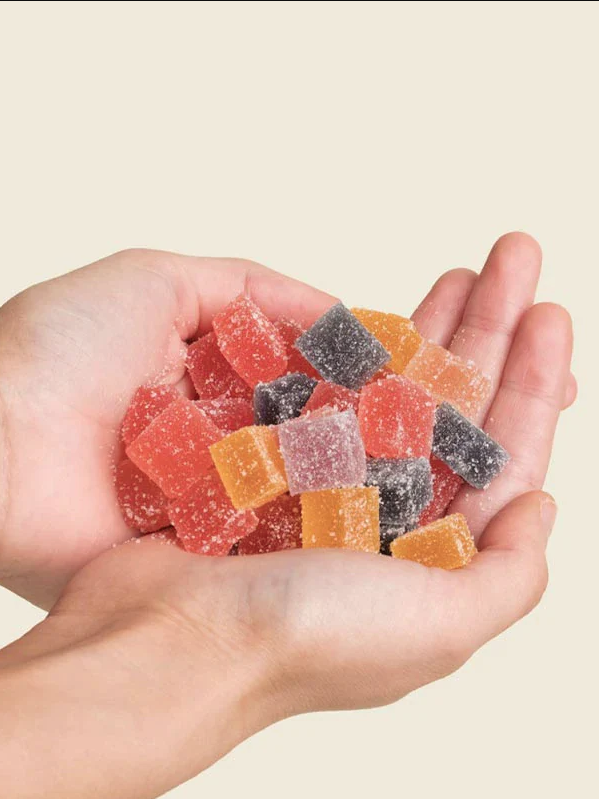 Two hands cupping colorful assorted sugar-coated jelly candies against a beige background.