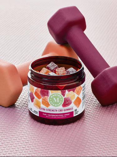 A jar of cbd gummies alongside two pink dumbbells and a peach-colored yoga block on a textured mat.
