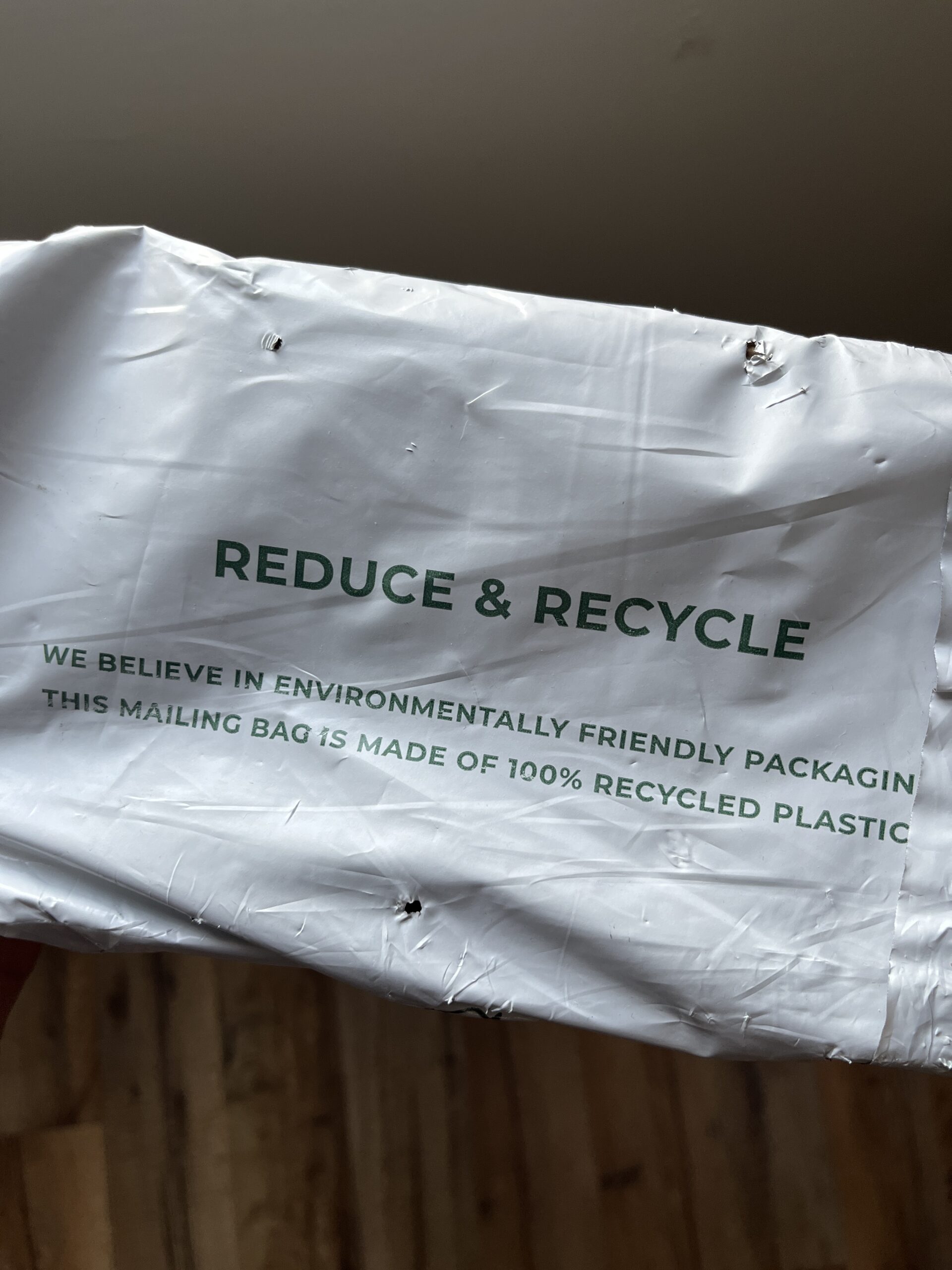 A crumpled mailing bag with "REDUCE & RECYCLE" printed on it. Below, a message reads, "WE BELIEVE IN ENVIRONMENTALLY FRIENDLY PACKAGING. THIS MAILING BAG IS MADE OF 100% RECYCLED PLASTIC.