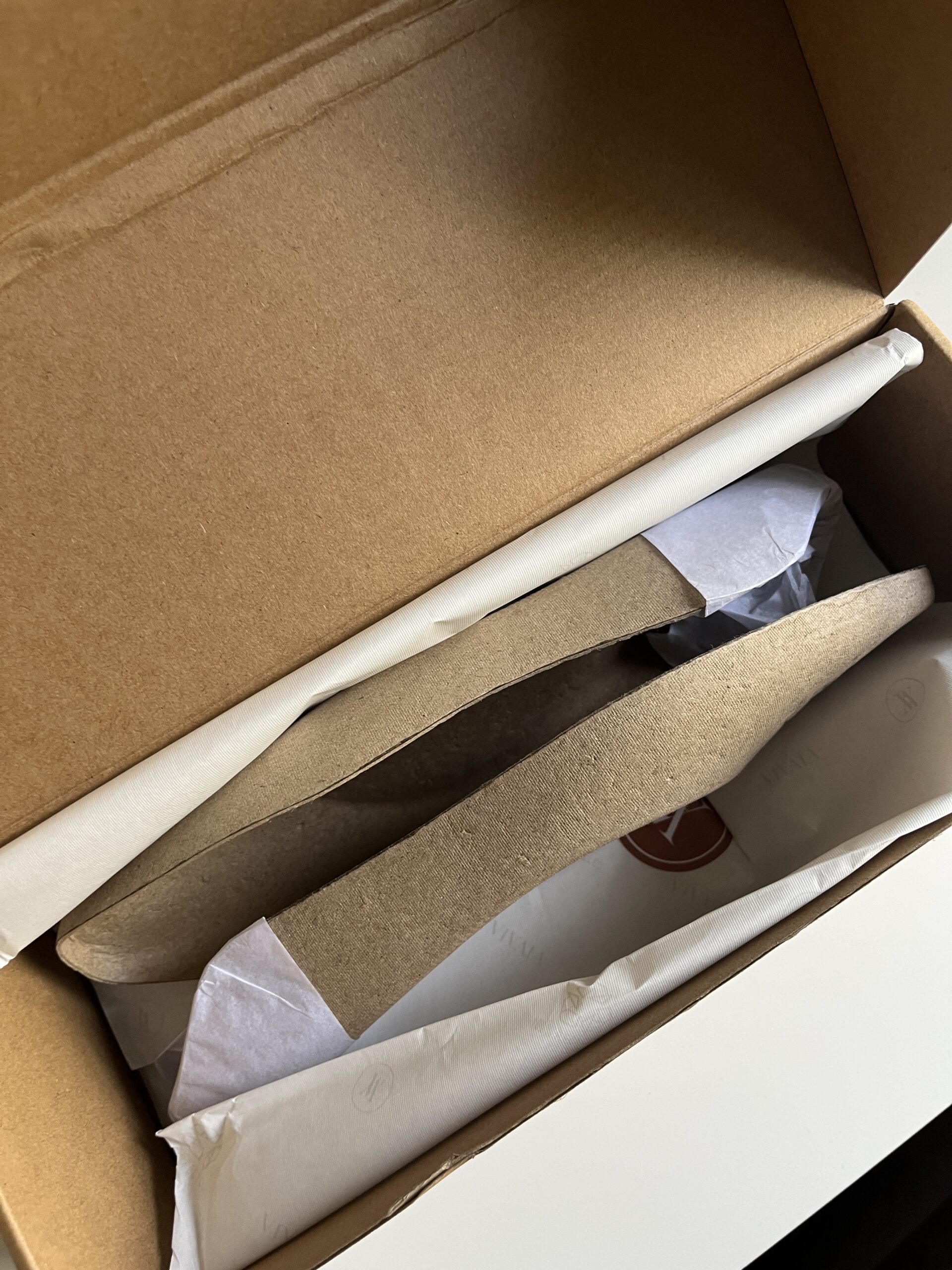 A cardboard box is partially open, revealing white tissue paper inside. The box is positioned on a white surface.