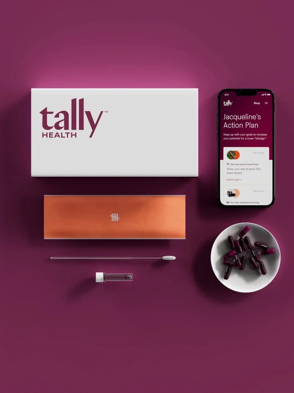 A Tally Health kit including a box, test tube, swab, pill container, bowl with capsules, and a phone displaying "Jacqueline's Action Plan" on a purple background.