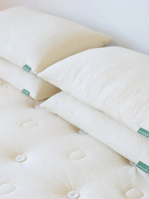 Four white bed pillows with green tags stacked in pairs on a mattress with button-tufted detailing.