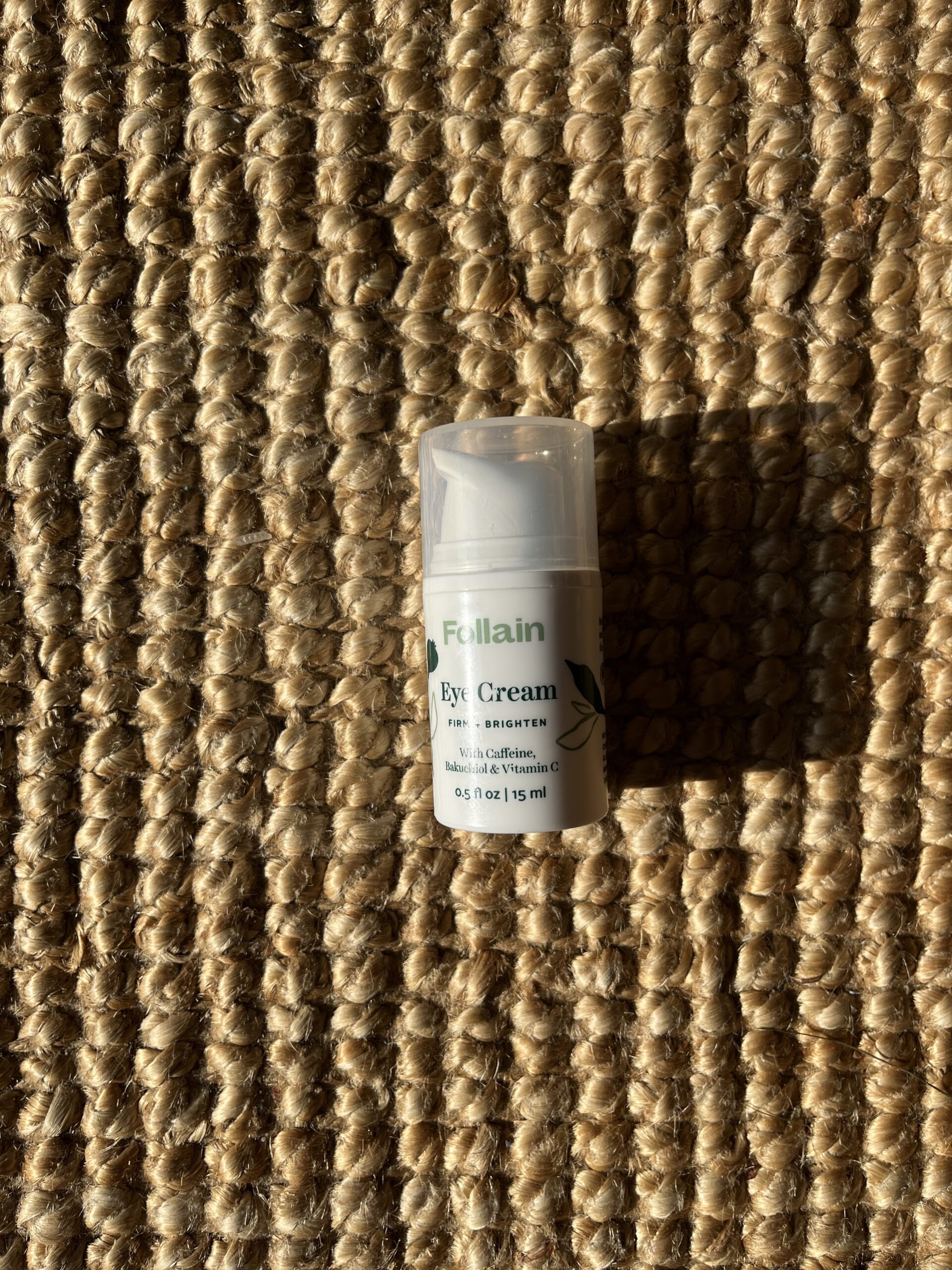 A small container of Follain Eye Cream with 15 ml, placed on a textured woven surface, lit with warm natural light.