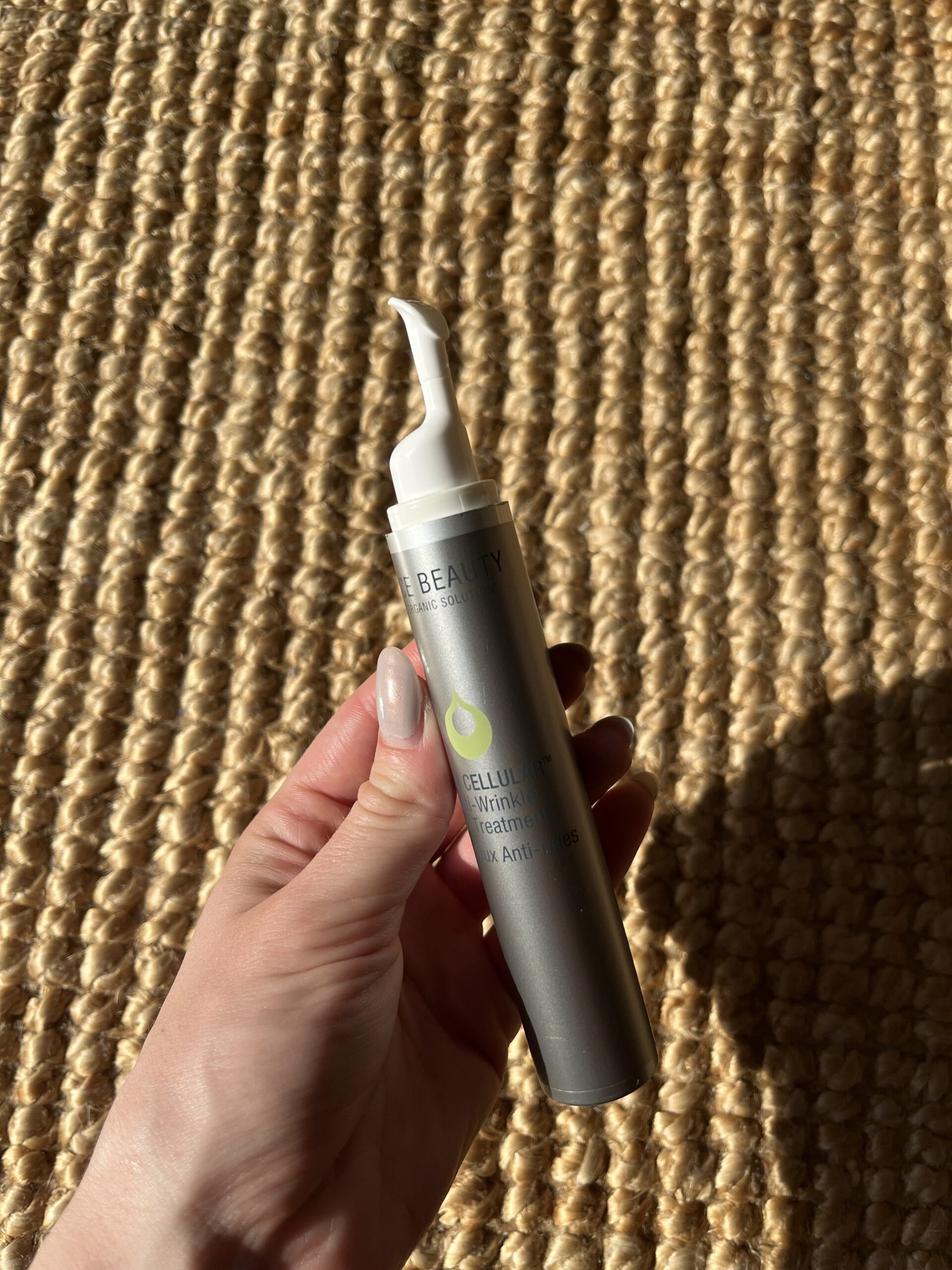 A hand holding a silver tube labeled "BEAUTY" with a white applicator tip against a textured background.