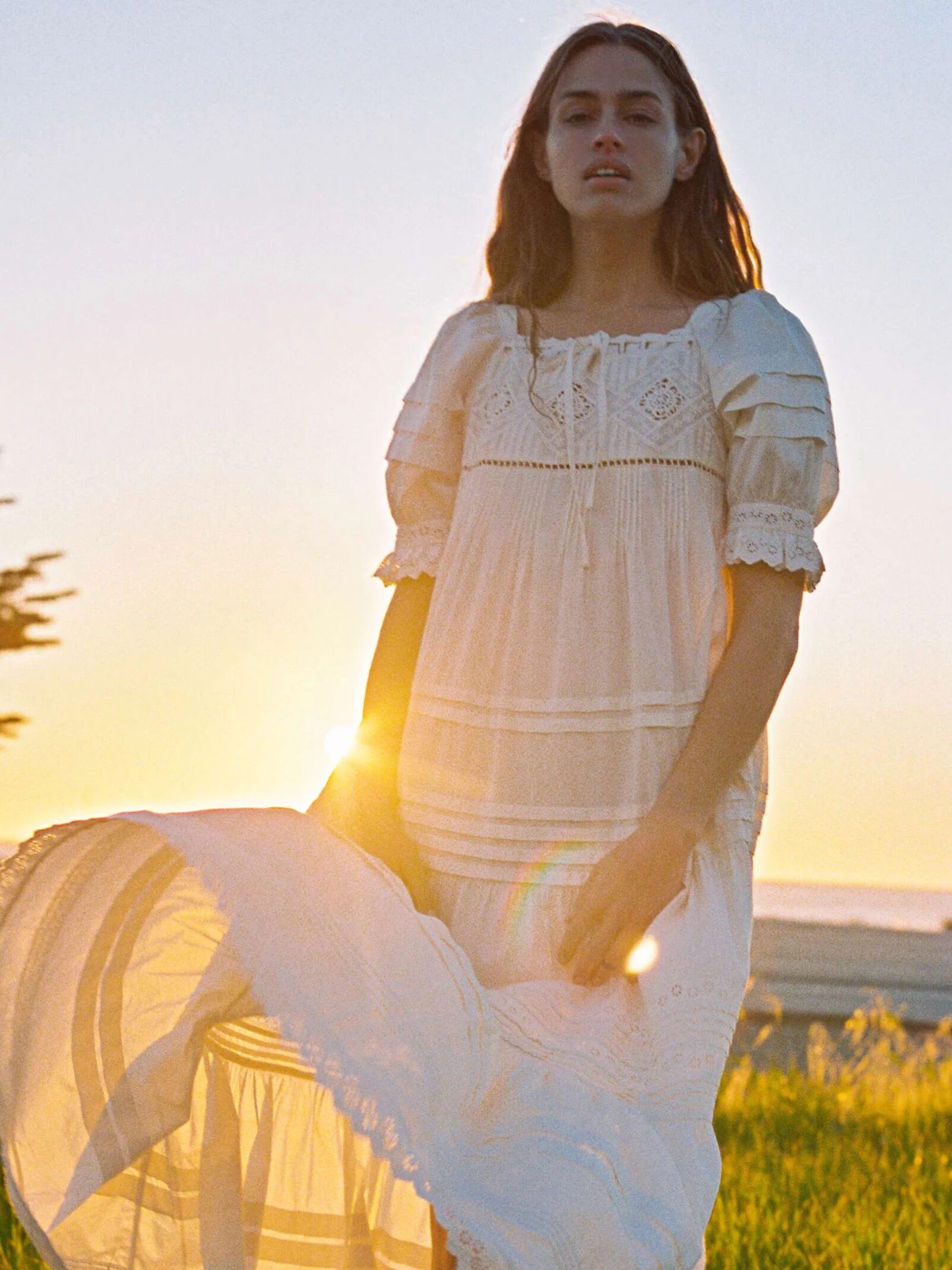 A model on a field wearing a short sleeve white maxi dress from Christy Dawn.