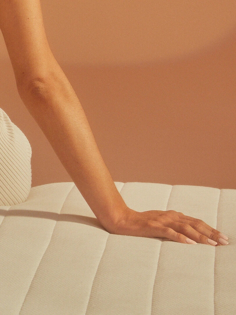 A person's hand and forearm rest on a padded, light-colored surface with a beige background.