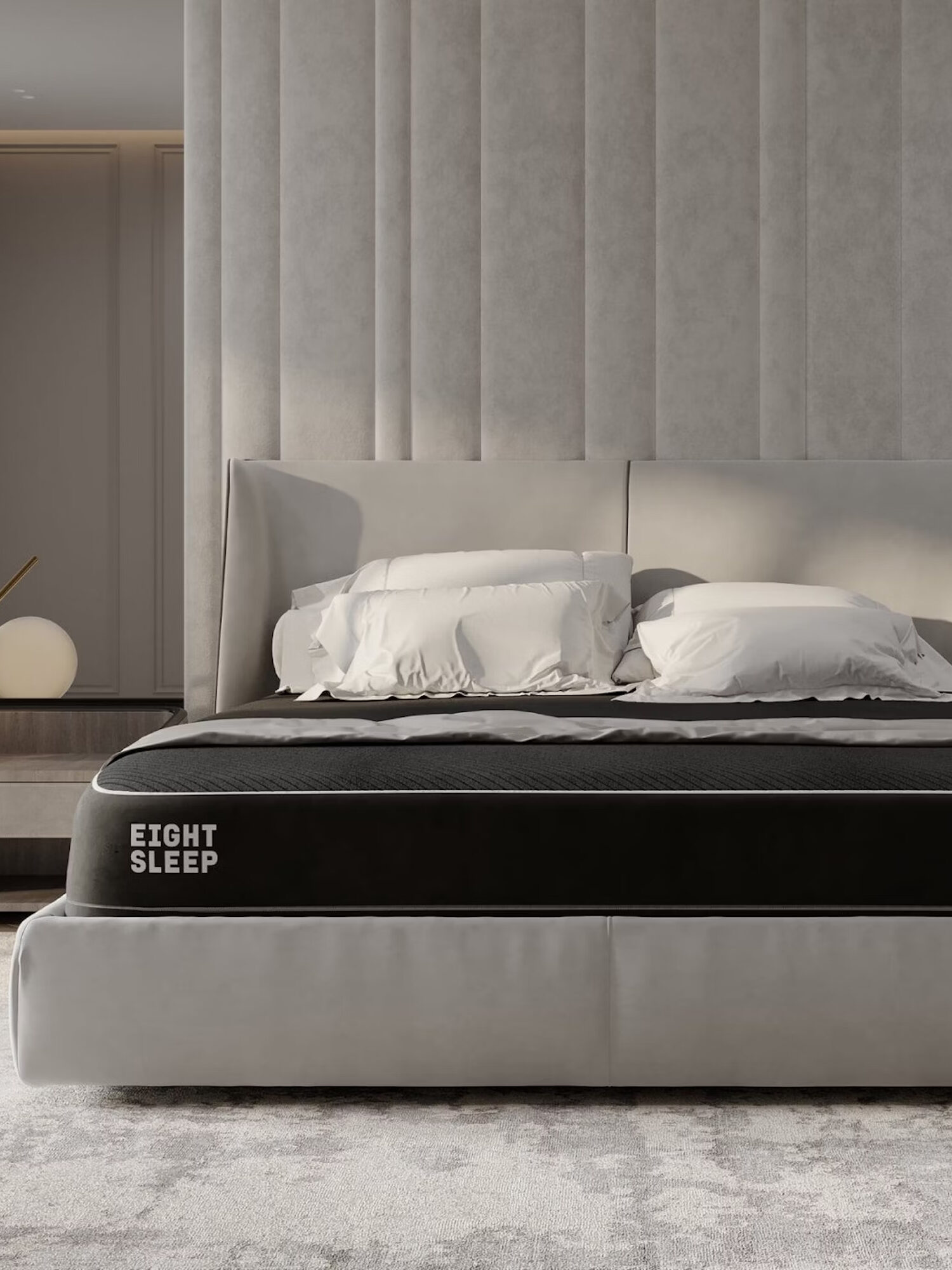 A modern bed features a headboard with vertical panels, two white pillows, and a dark mattress labeled "EIGHT SLEEP." The bed is set in a neutral-toned bedroom with minimalist decor.