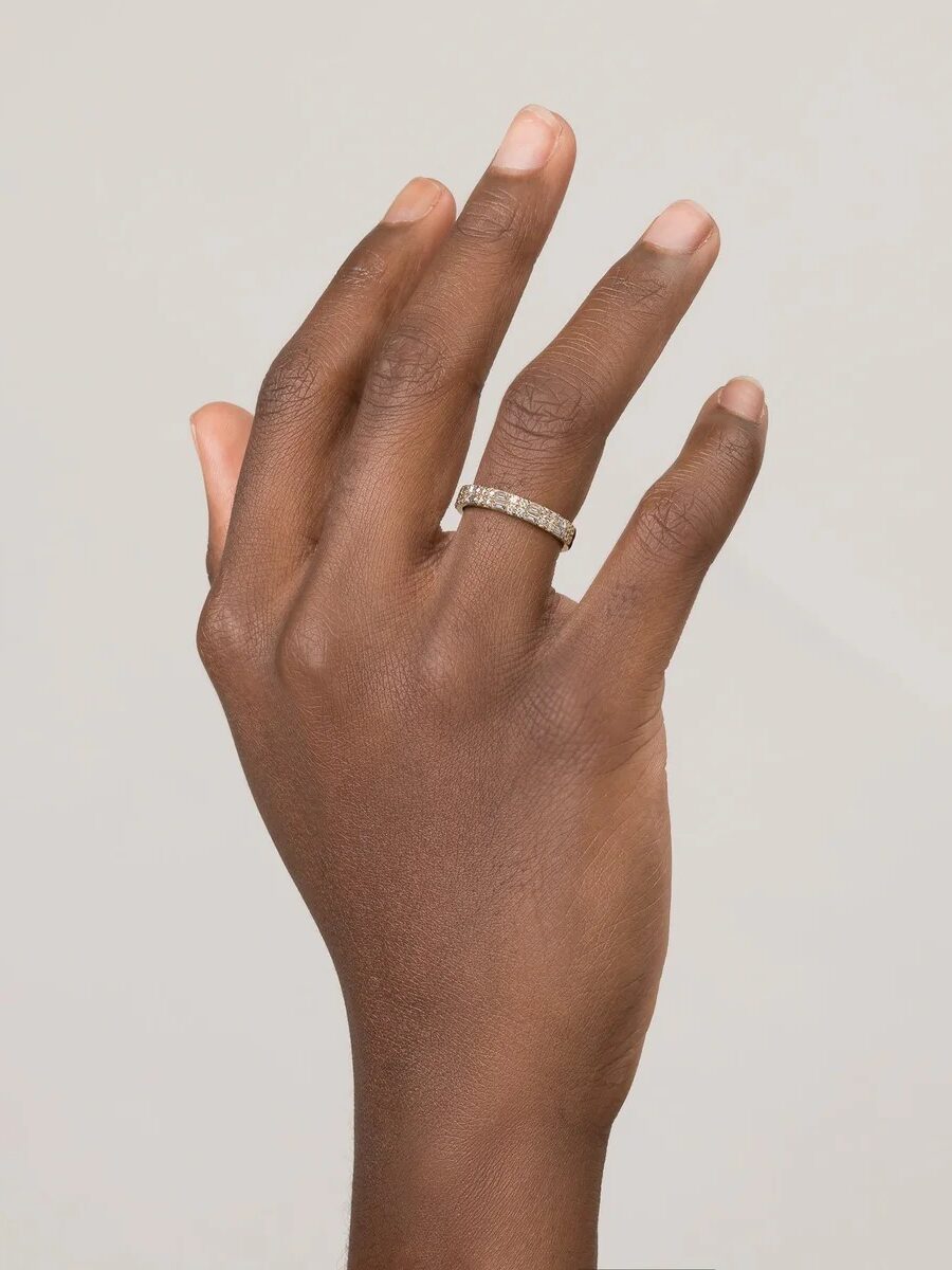 A hand adorned with a gold ring with small gemstones on the ring finger, shown against a plain light background.