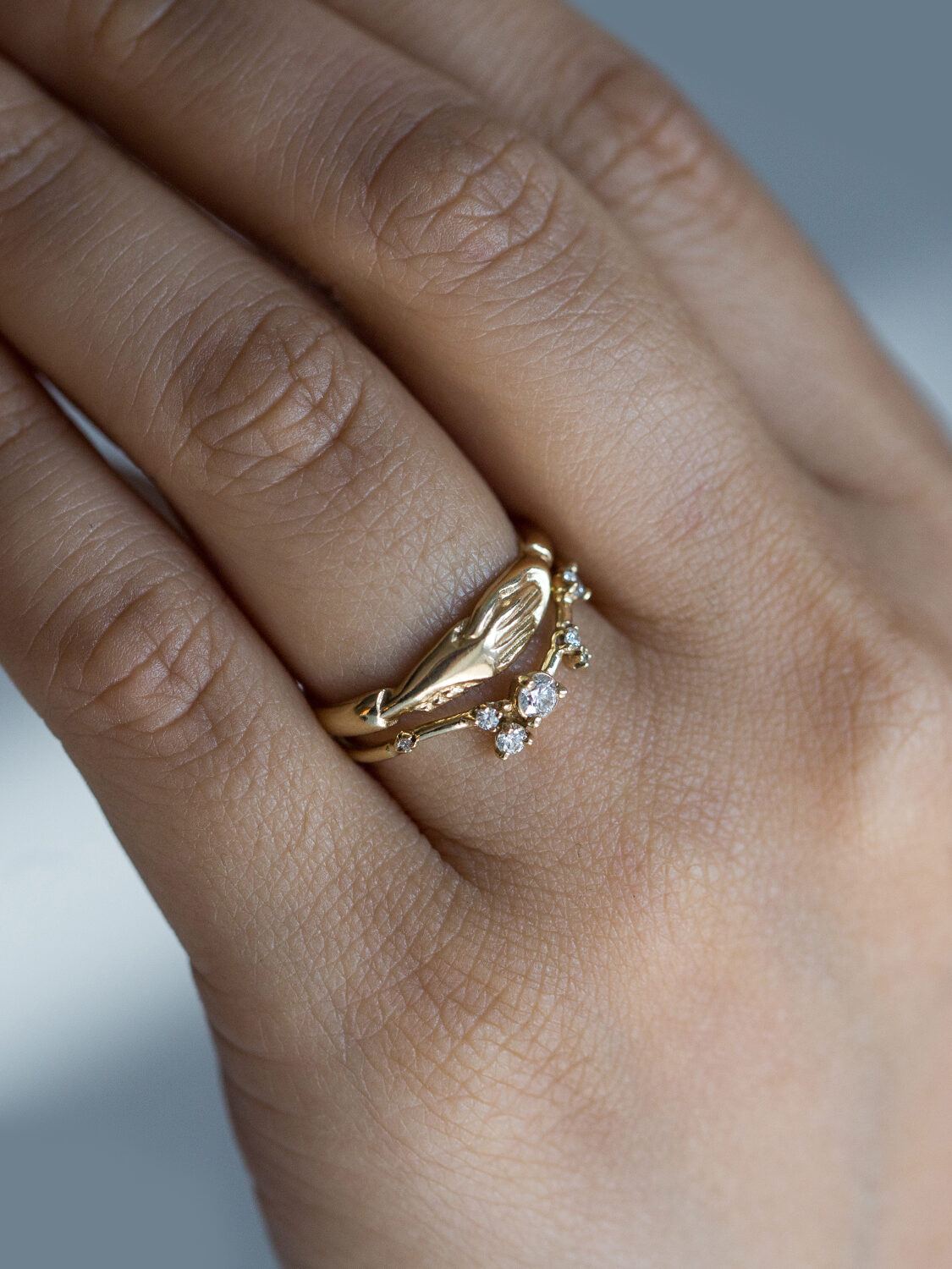 A hand wears two gold rings with one featuring four small, round diamonds.