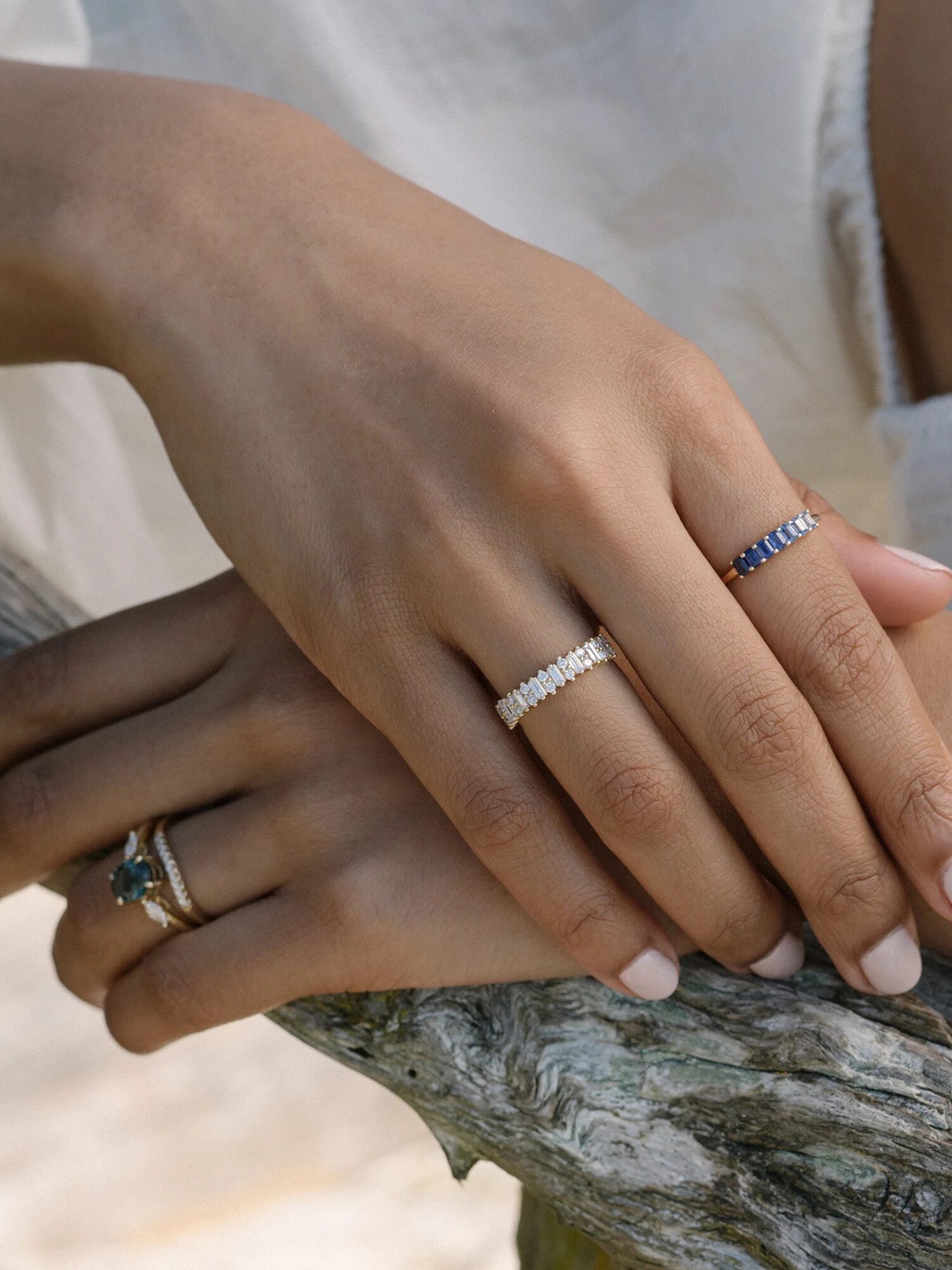 Close-up of a person’s hands wearing four different rings, featuring various gemstones, resting on a weathered wooden surface.