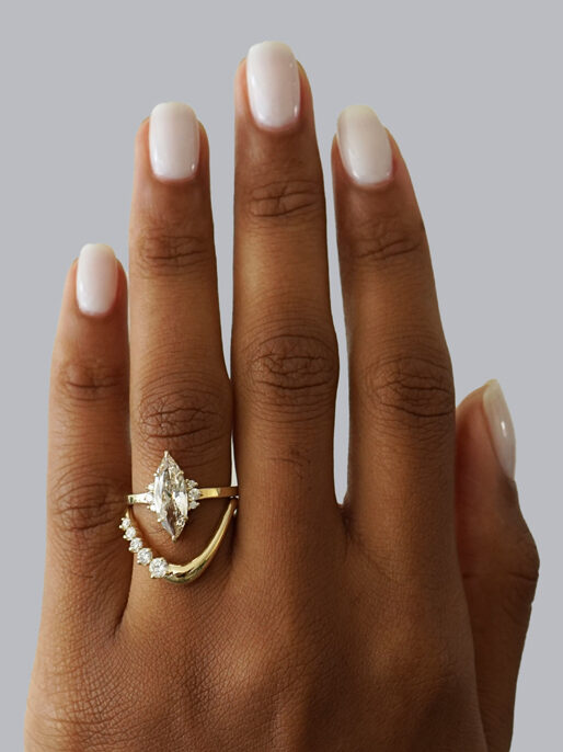 A hand with neatly manicured nails displays two gold rings, one featuring a marquise-cut diamond and the other adorned with smaller diamonds.