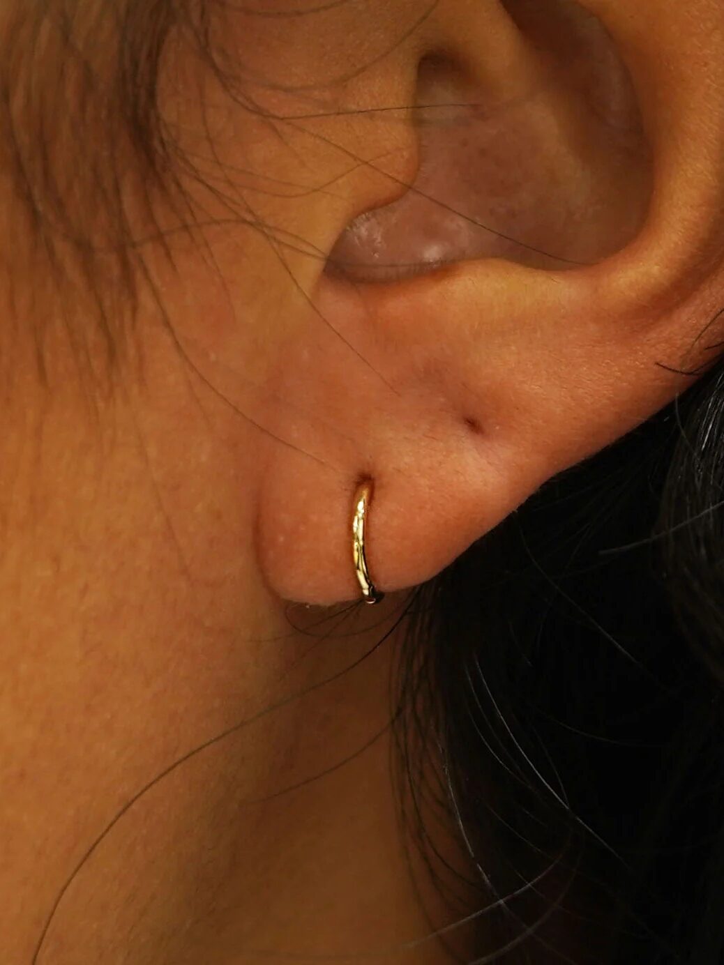 Close-up of a person's ear wearing a small gold hoop earring.