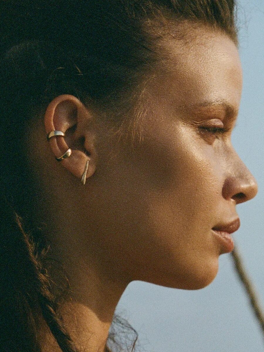 Profile of a woman with a serene expression, wearing minimalist gold earrings, against a soft-focus background during twilight.