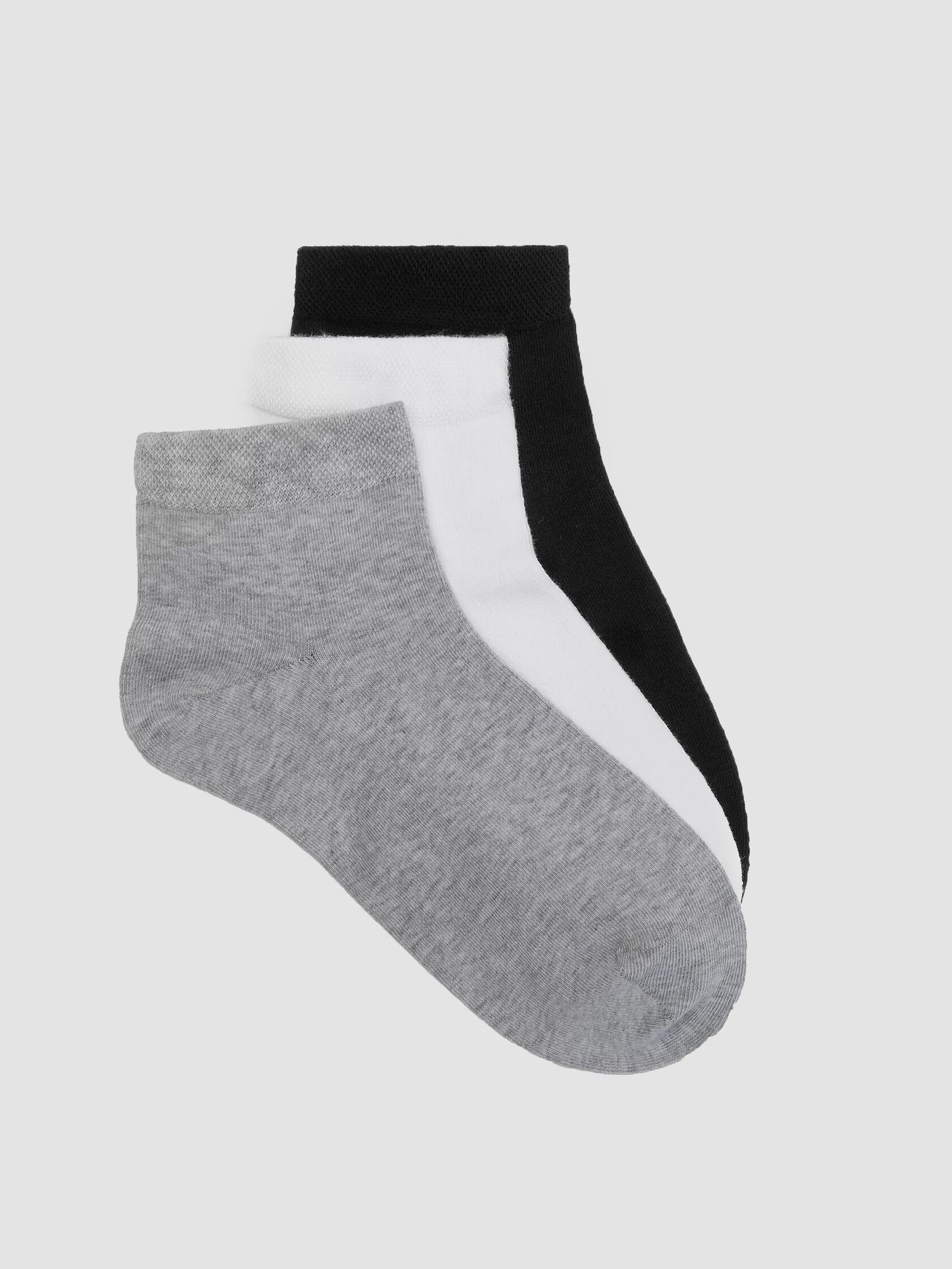 Three pairs of plain ankle socks in black, white, and grey, made from organic materials, stacked together on a plain background.