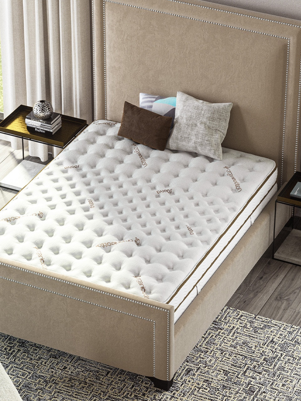 A neatly made bed with a beige upholstered frame, layered with a white textured mattress, two pillows, one brown and one white. The room features side tables and a carpet over a wooden floor.