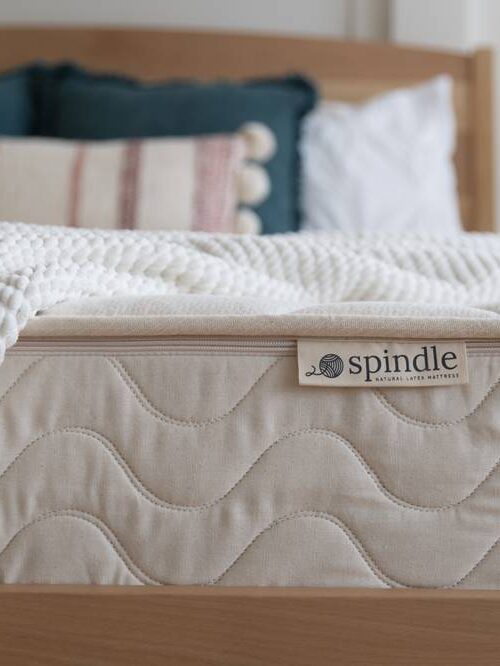 A neatly made bed with a Spindle mattress and white textured blanket, featuring a wooden headboard and decorative pillows in the background.