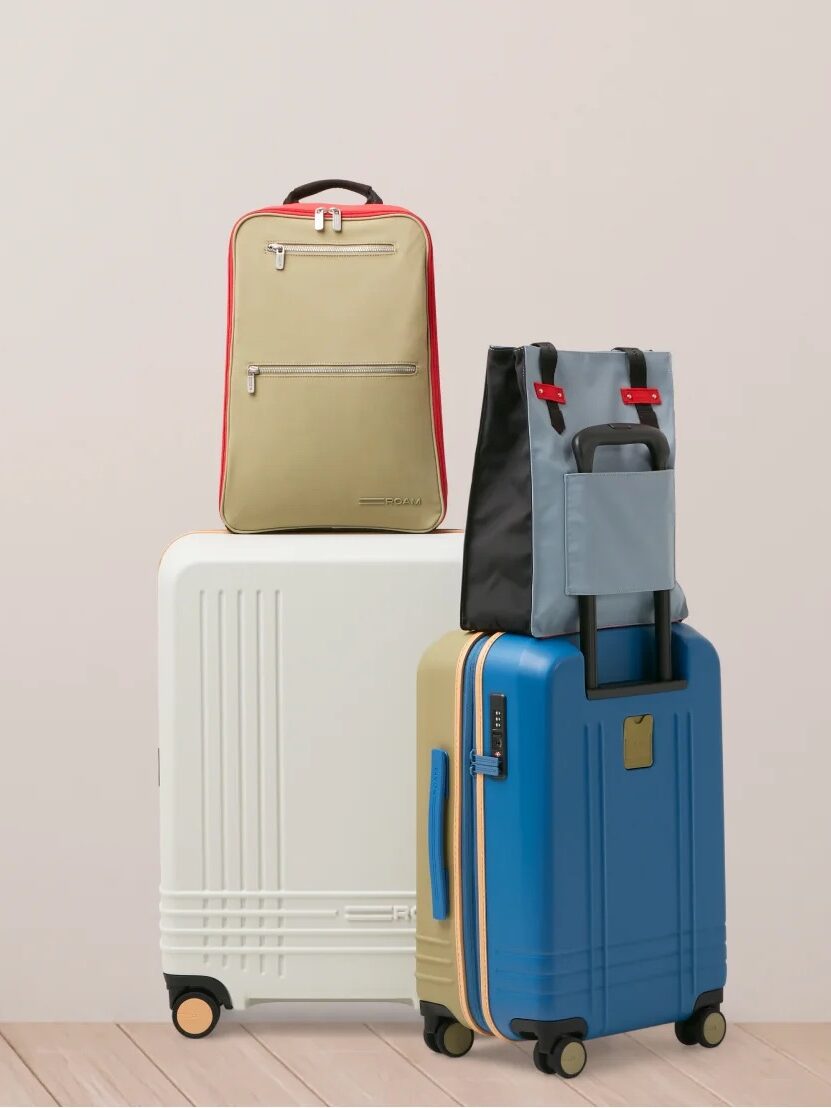 Three suitcases, one red, one white, and one blue, stacked vertically and leaning on each other against a plain wall on a wooden floor.