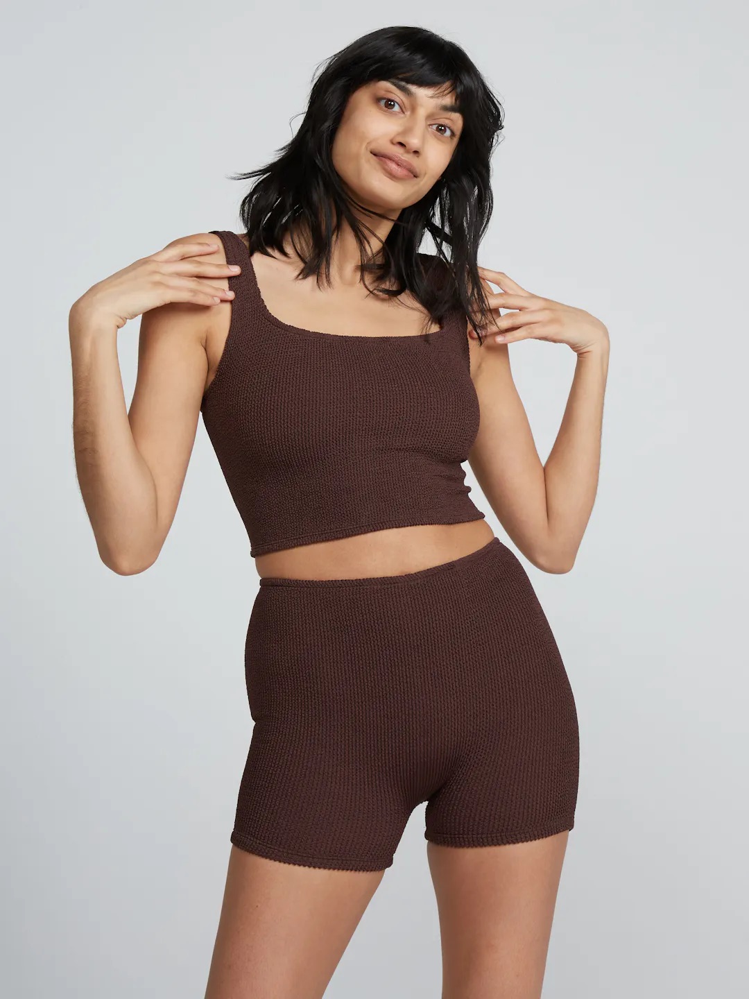 A woman poses wearing a matching brown knit tank top and shorts set against a plain background.