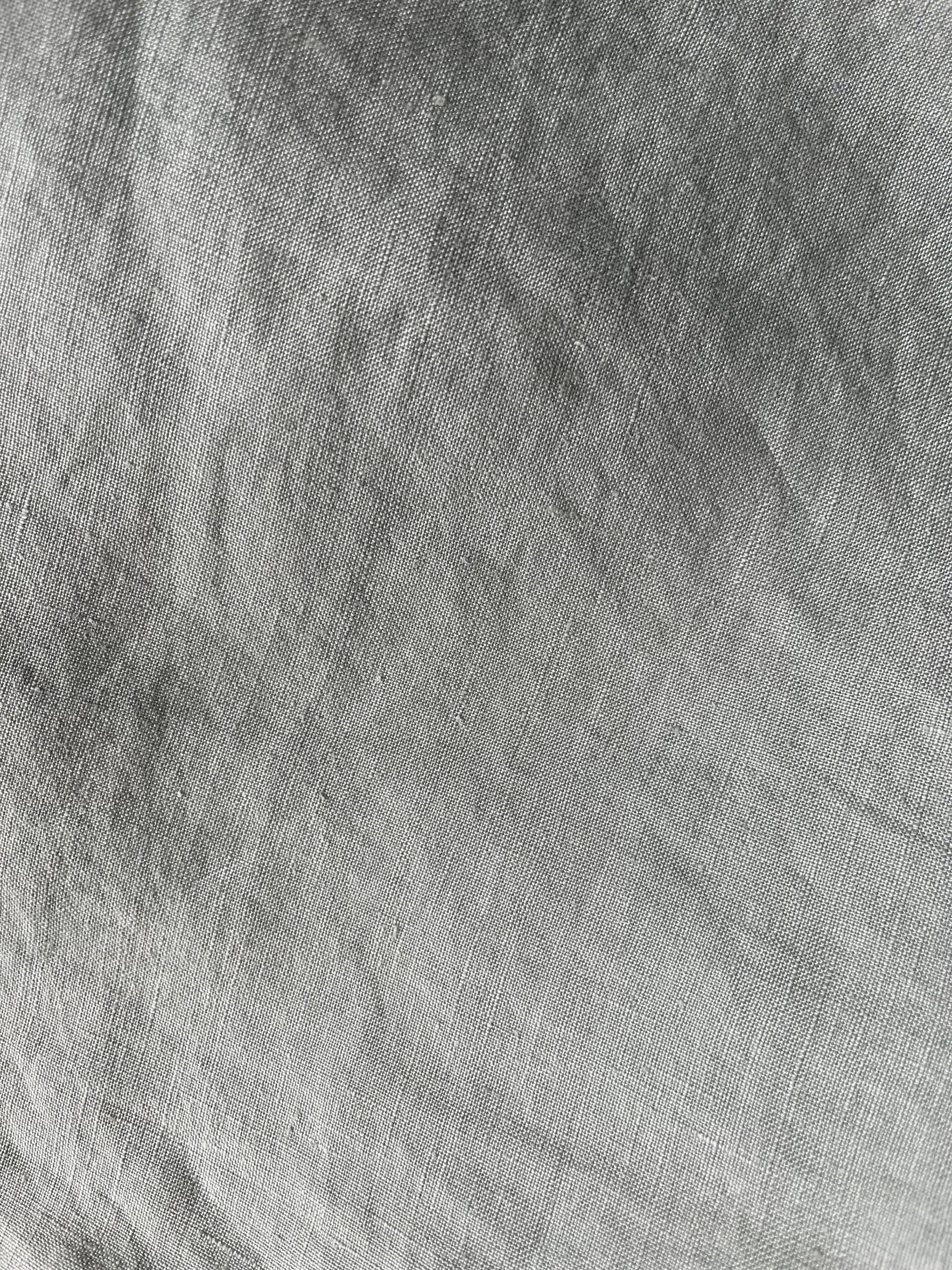 Close-up image of a grey fabric texture with visible weave patterns and slight variations in shading.