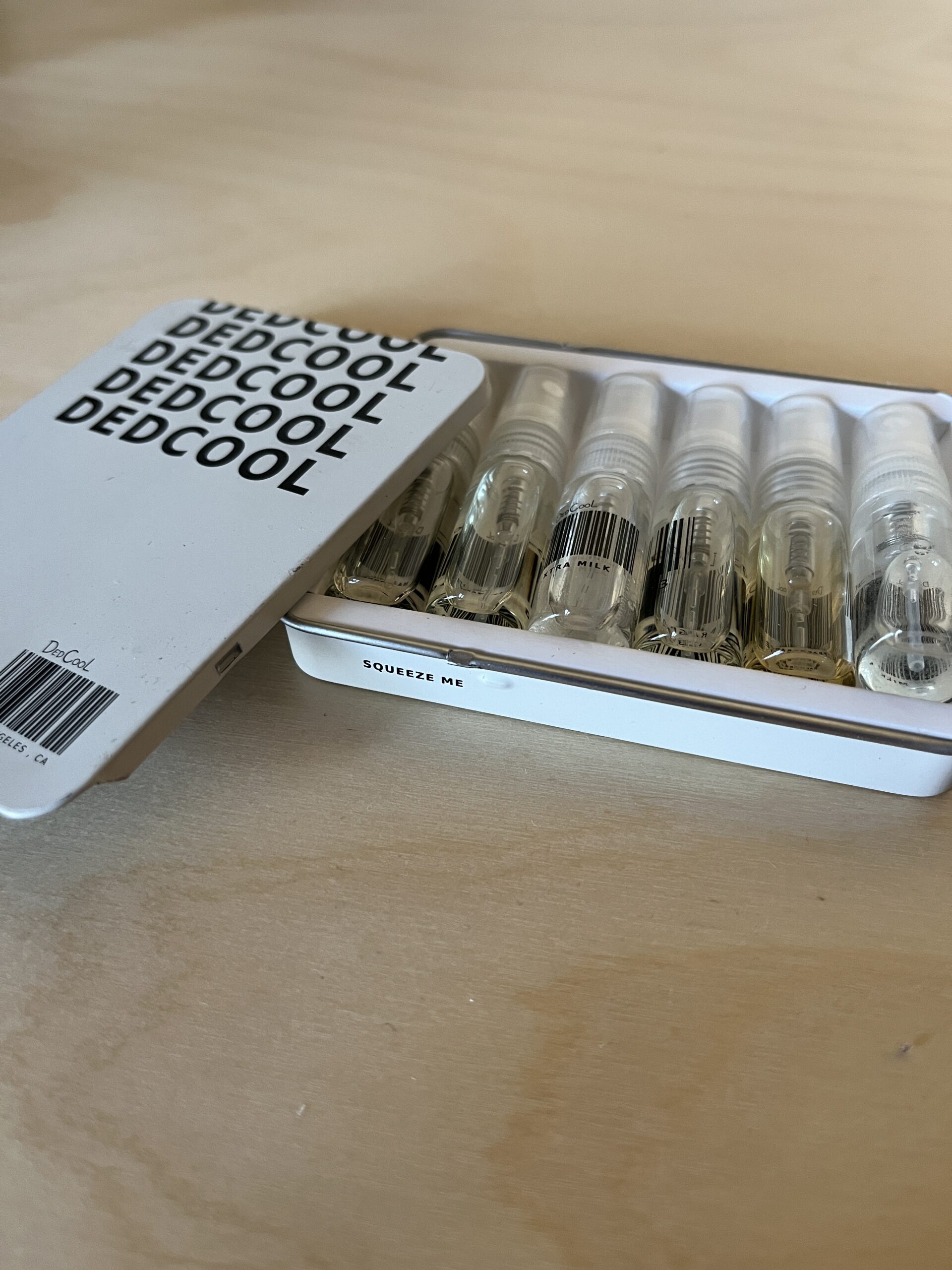 A white box labeled "Dedcool" contains six small spray bottles. The lid is partially open, showing the bottles inside.