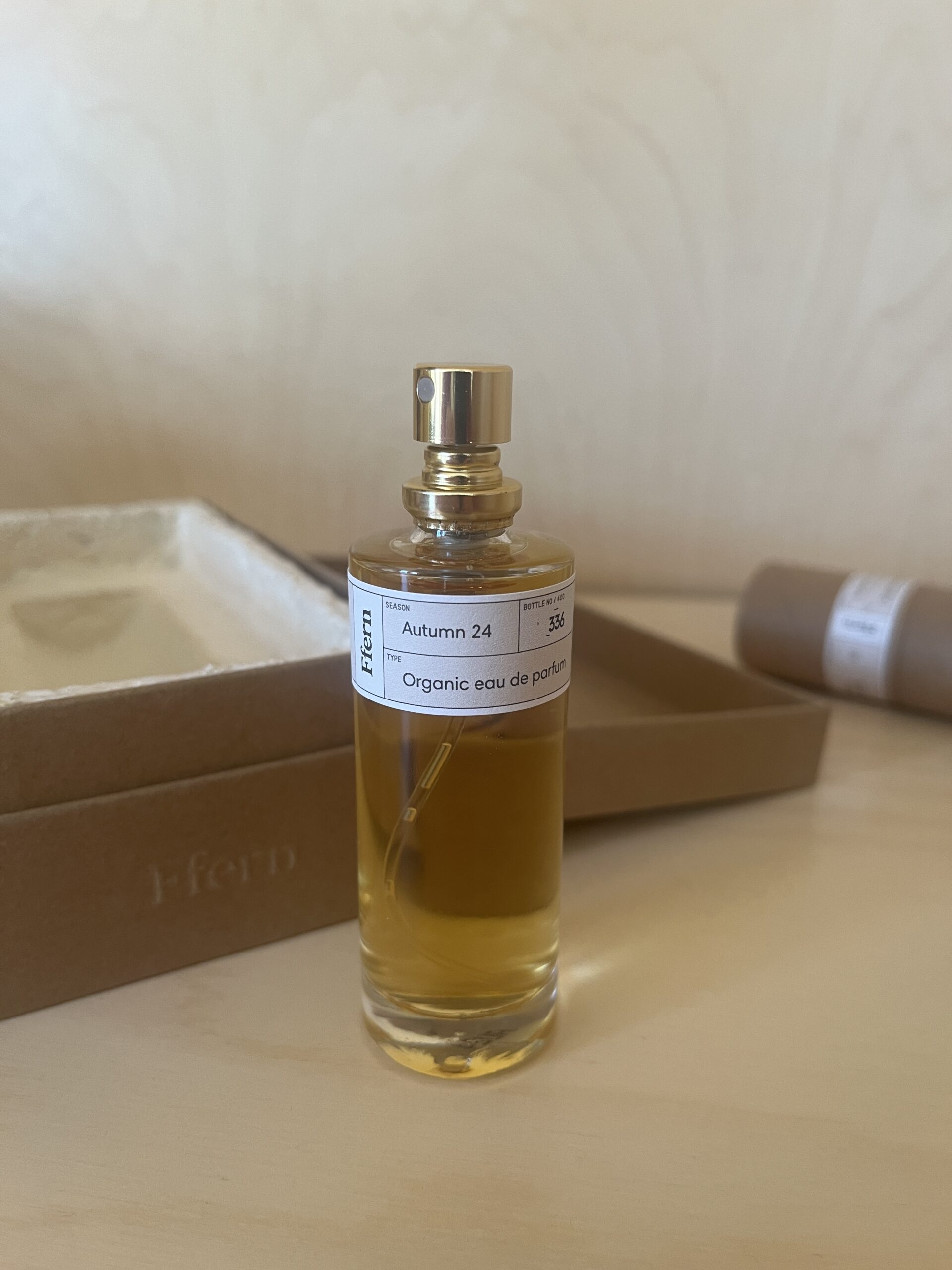 A glass bottle of "Autumn 24" organic eau de parfum with a spray nozzle is placed in front of an open, rectangular cardboard box.