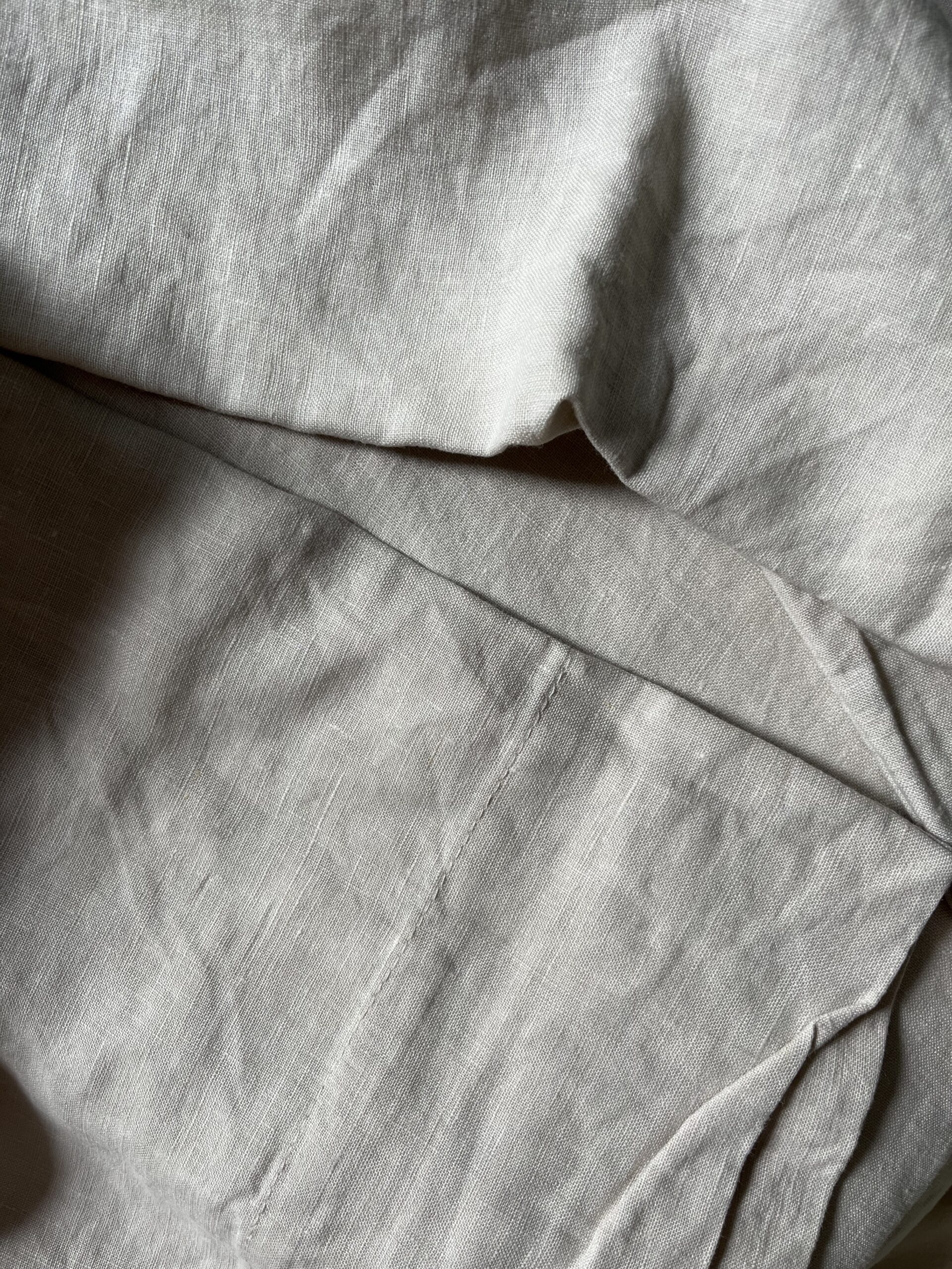 Close-up image of rumpled, light-colored fabric with visible stitching and texture.