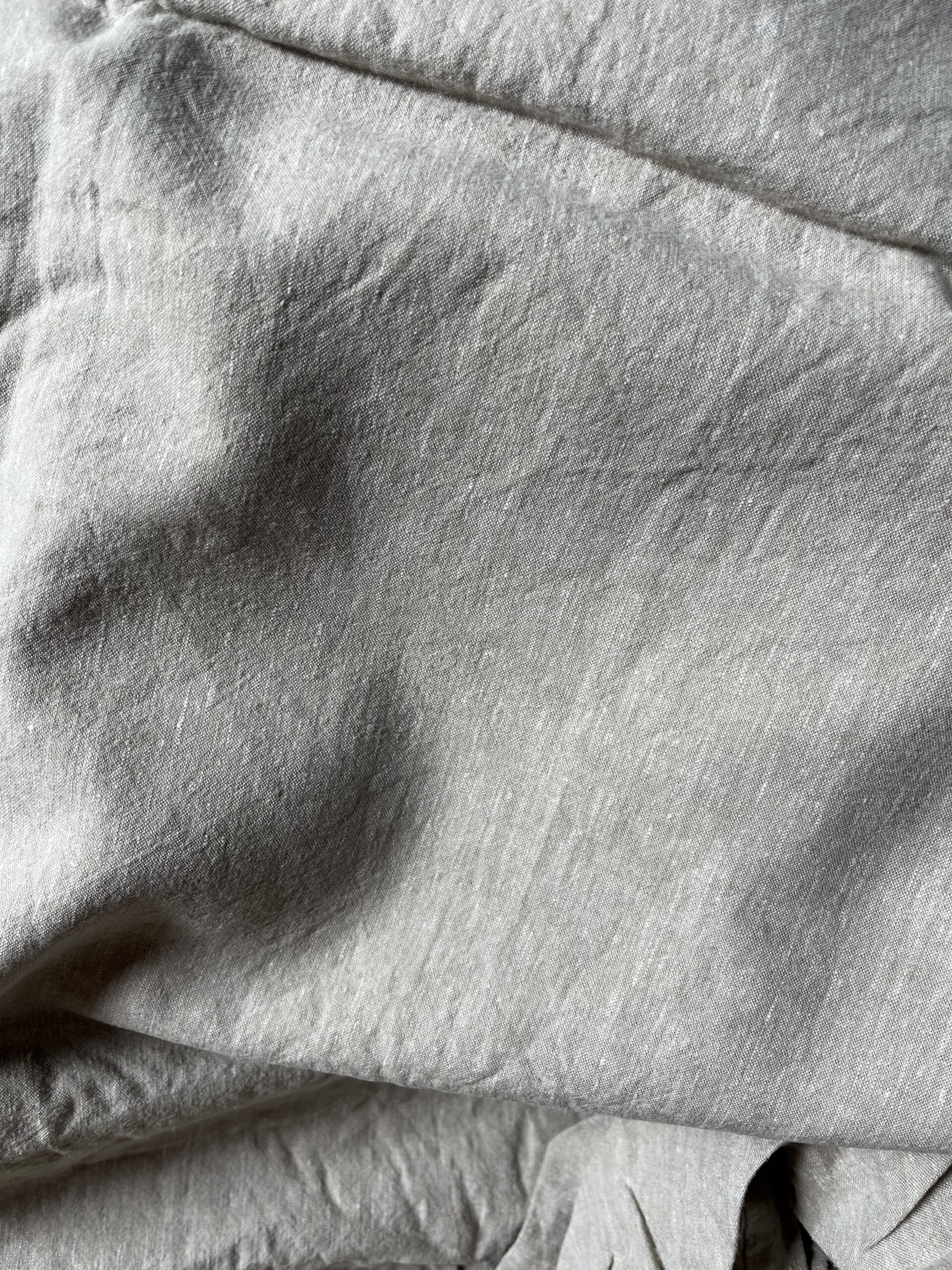 Close-up view of a crumpled, light grey fabric, displaying its texture and weave pattern.
