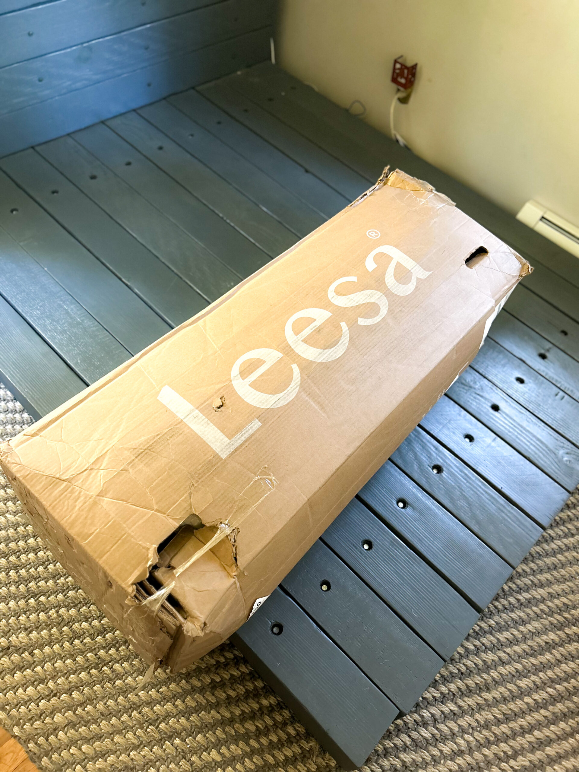 A slightly damaged cardboard box labeled "Leesa" sits on a partially assembled bed frame.