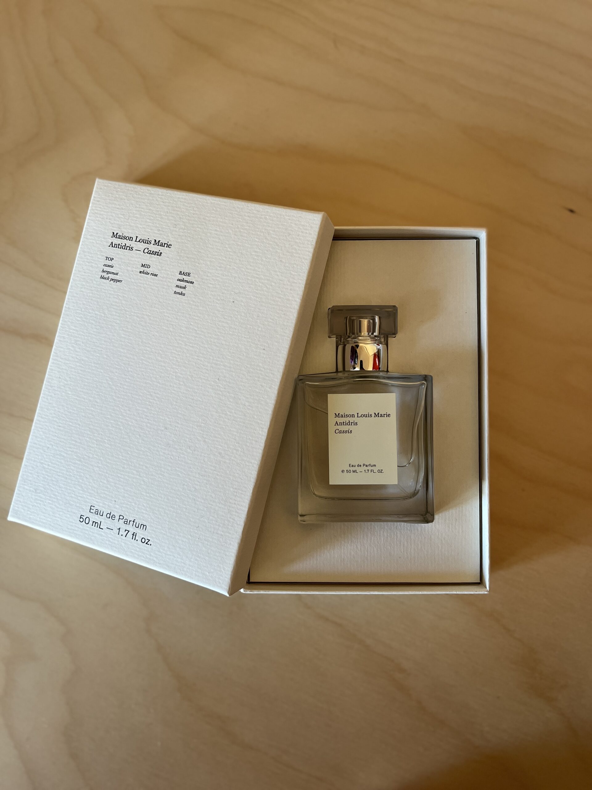 A clear glass bottle of Maison Louis Marie perfume in an open white box sits on a wooden surface.