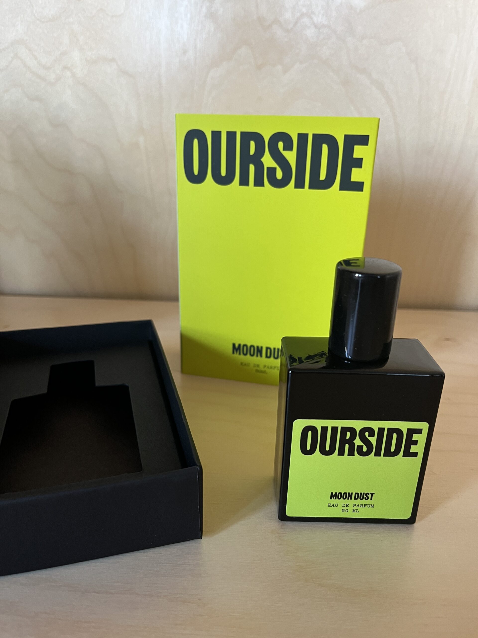 Perfume bottle labeled "Ourside Moon Dust" with matching yellow box on a wooden surface.