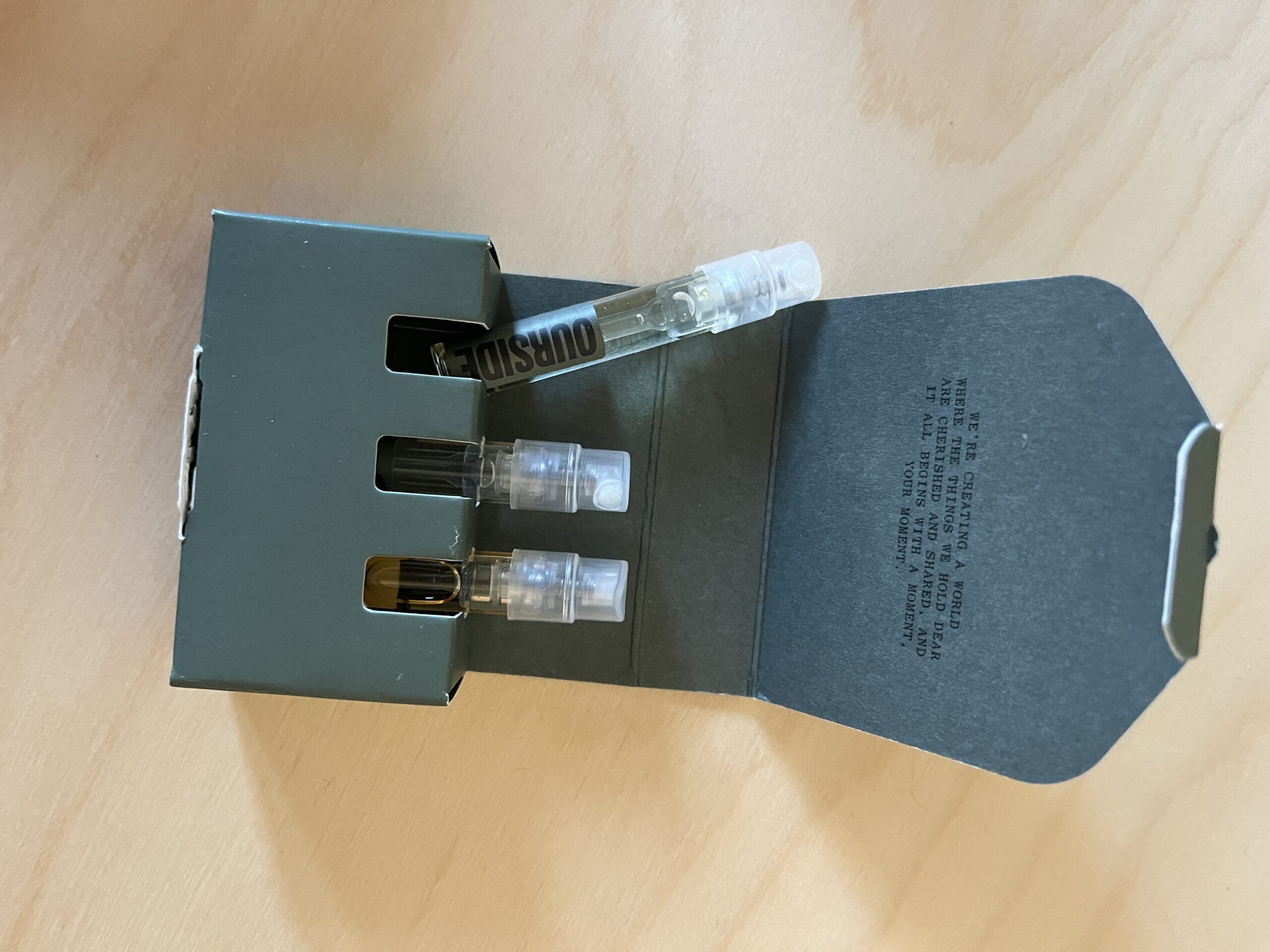 A partially open black box containing three transparent spray vials lies on a wooden surface.